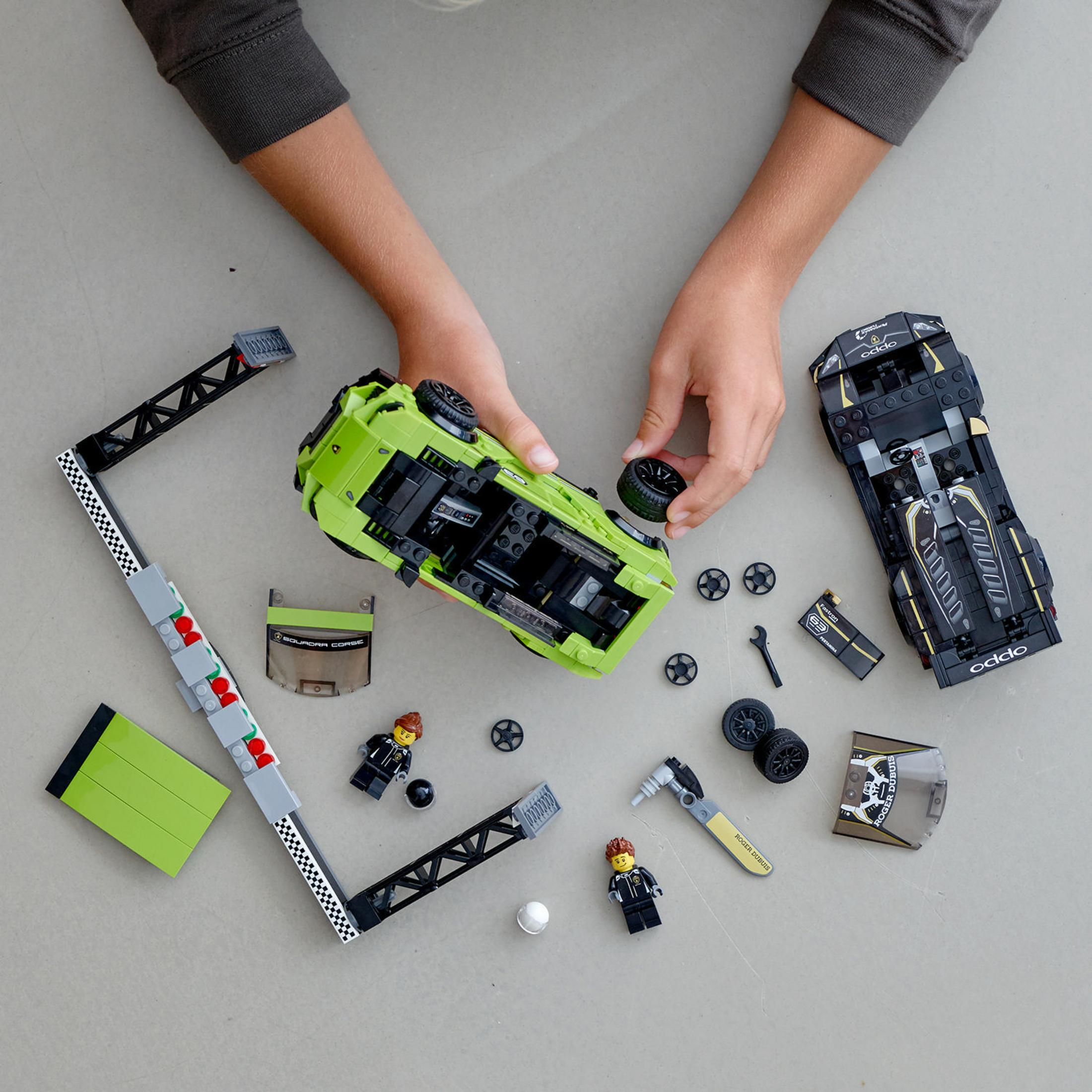 Hands assembling Lego car with tools and other Lego parts on a light gray surface.