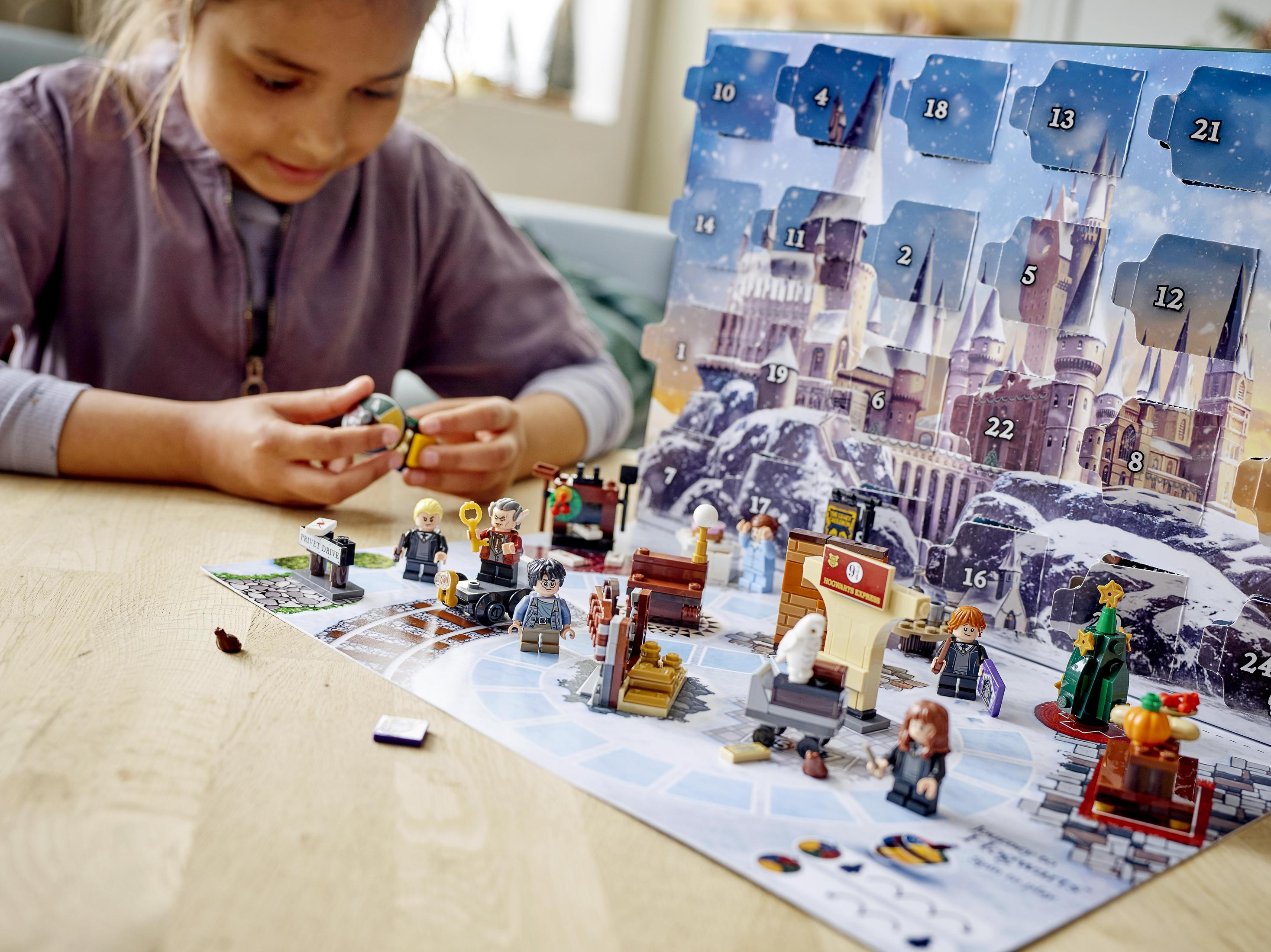 Mädchen spielt mit einem Lego Harry Potter Adventskalender. Figuren sind auf einer Tafel mit Hogwarts abgebildet.