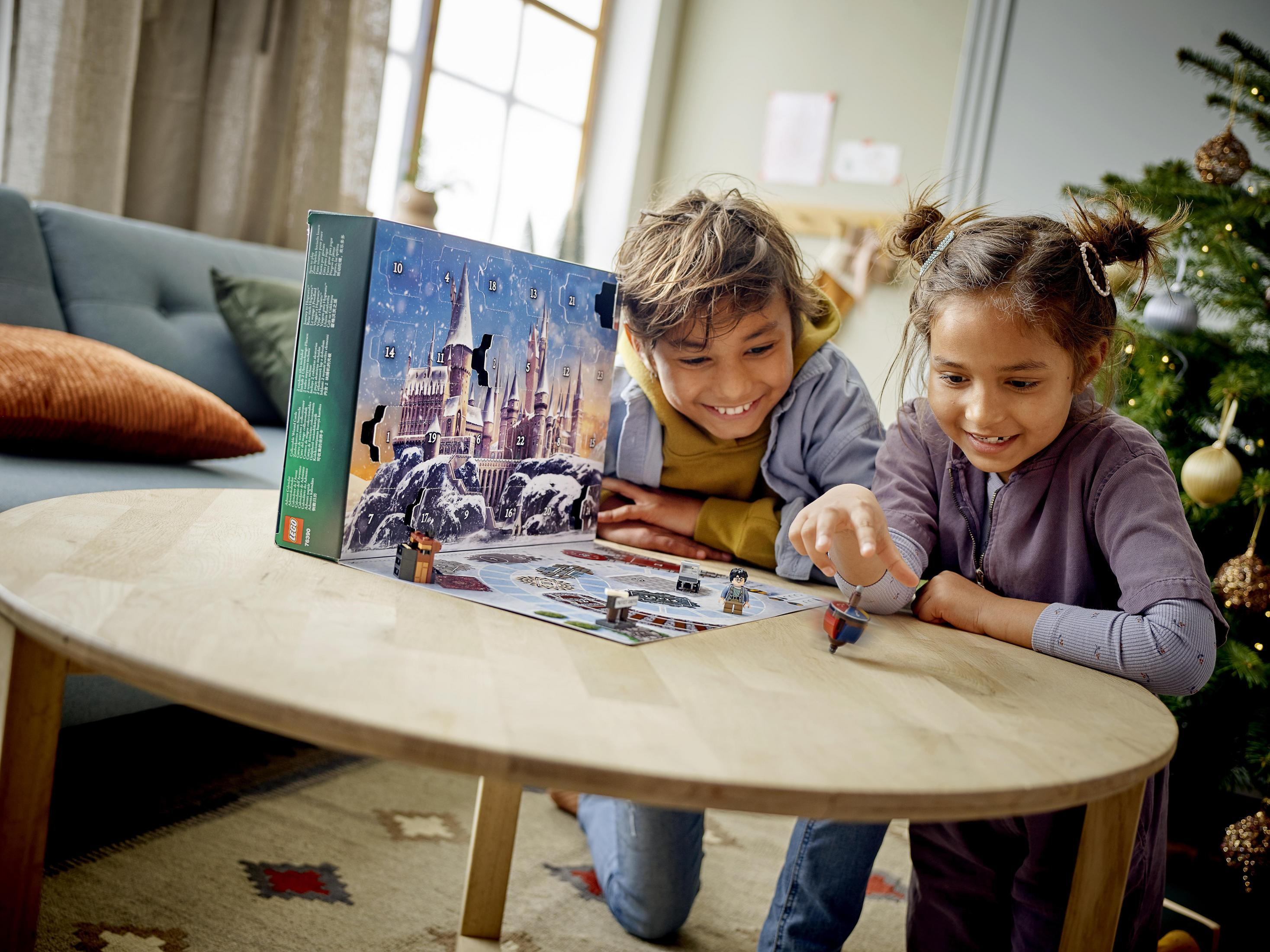 Zwei Kinder spielen ein Brettspiel. Eines zeigt. Weihnachtsbaum im Hintergrund.