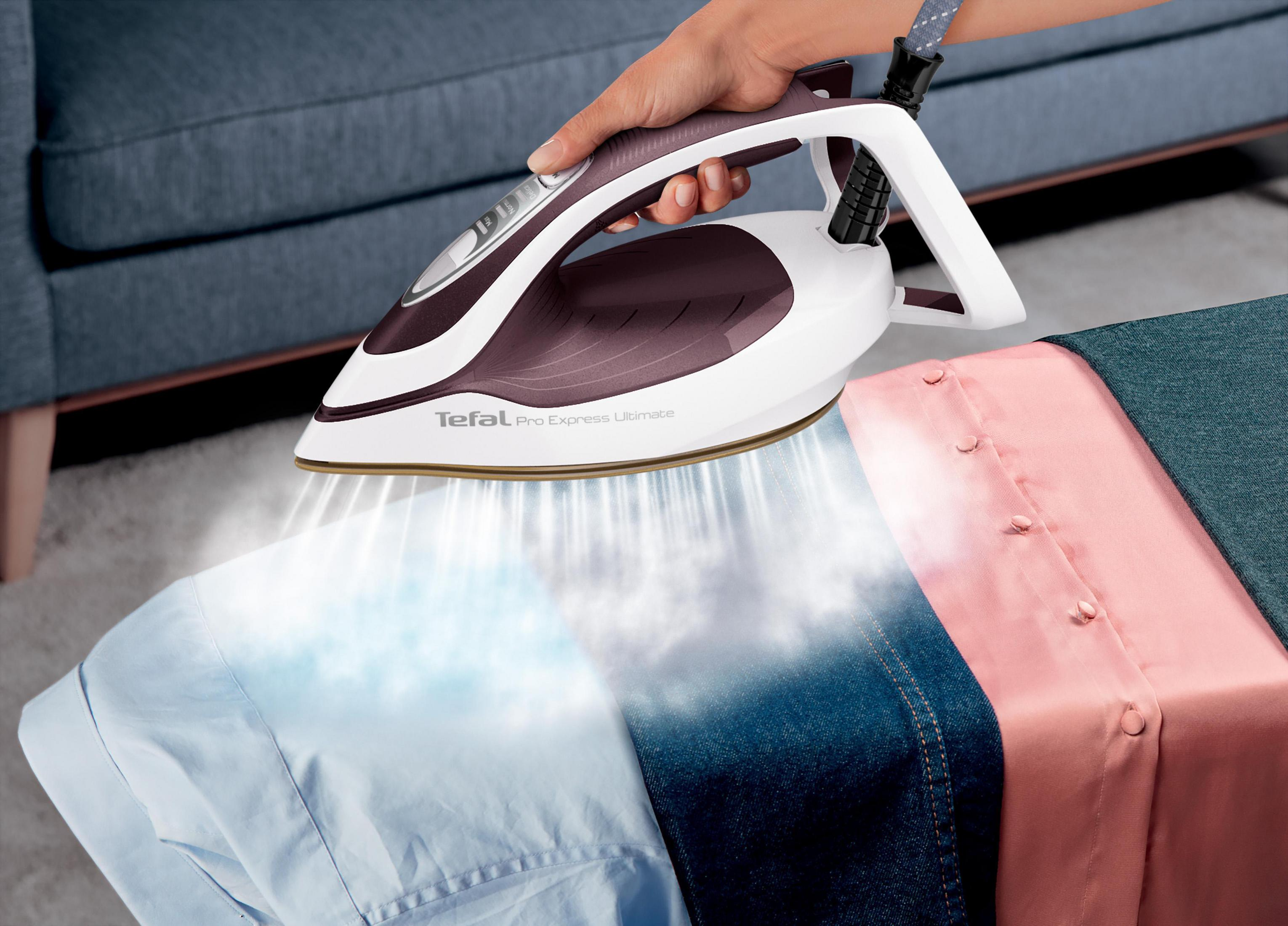 Ręka prasująca tkaninę białym i fioletowym żelazkiem, widoczna para.