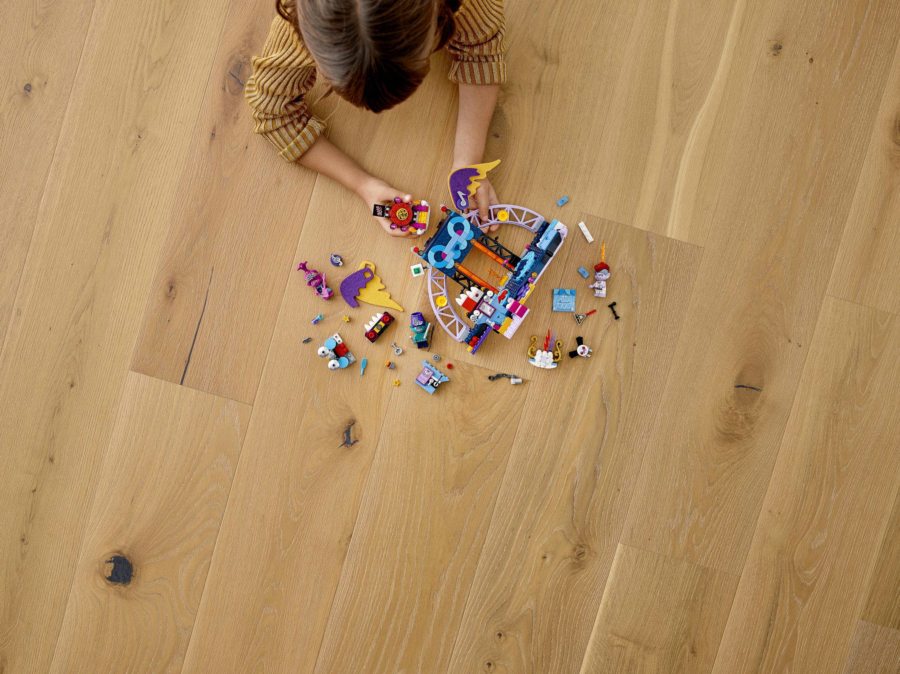 Ein Kind, das auf einem Holzboden liegt und mit einem Spielzeugset spielt, Draufsicht.