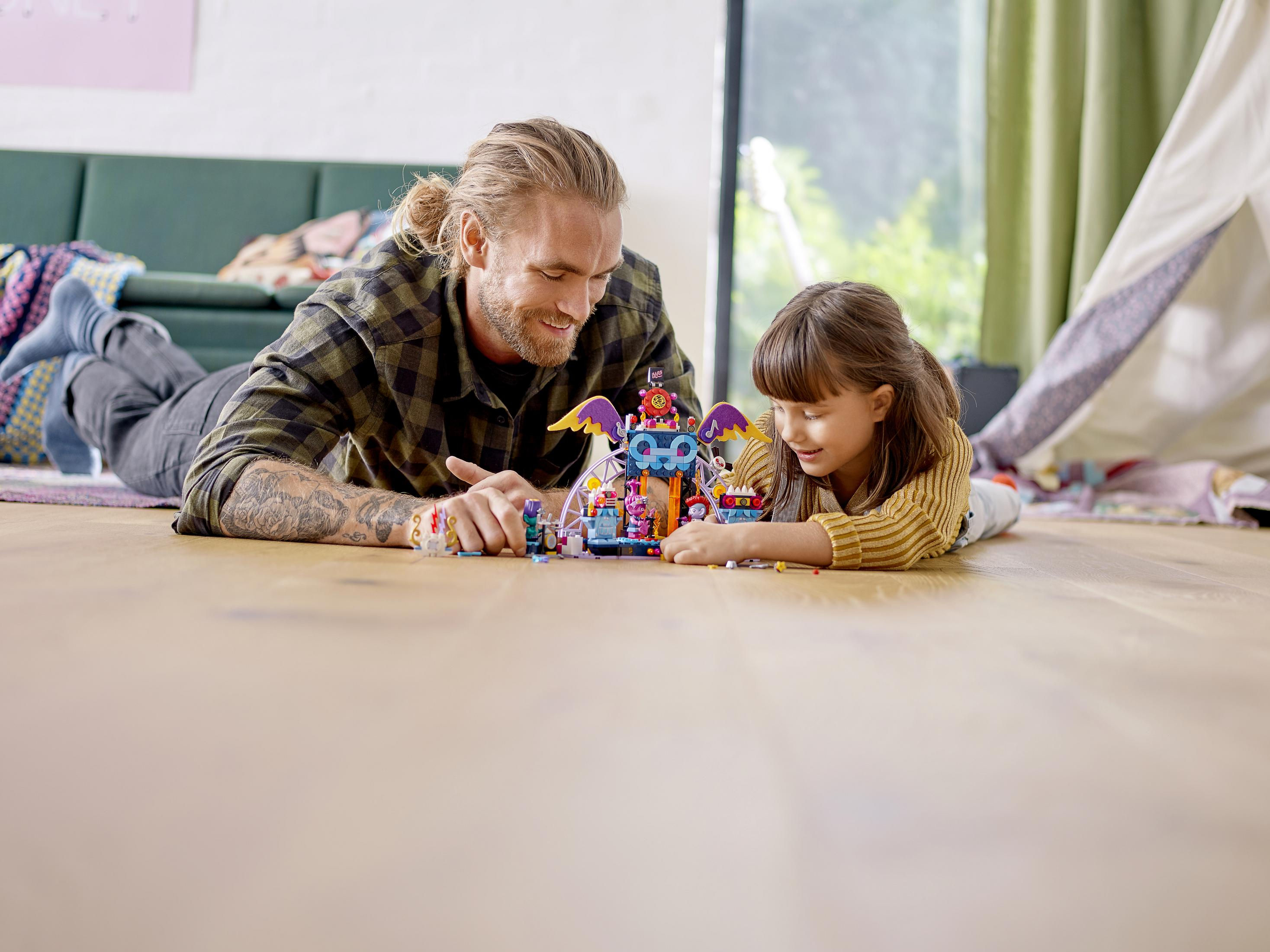 Ein Vater und eine Tochter bauen gemeinsam eine Spielzeugburg, liegen zusammen auf dem Boden und lächeln.