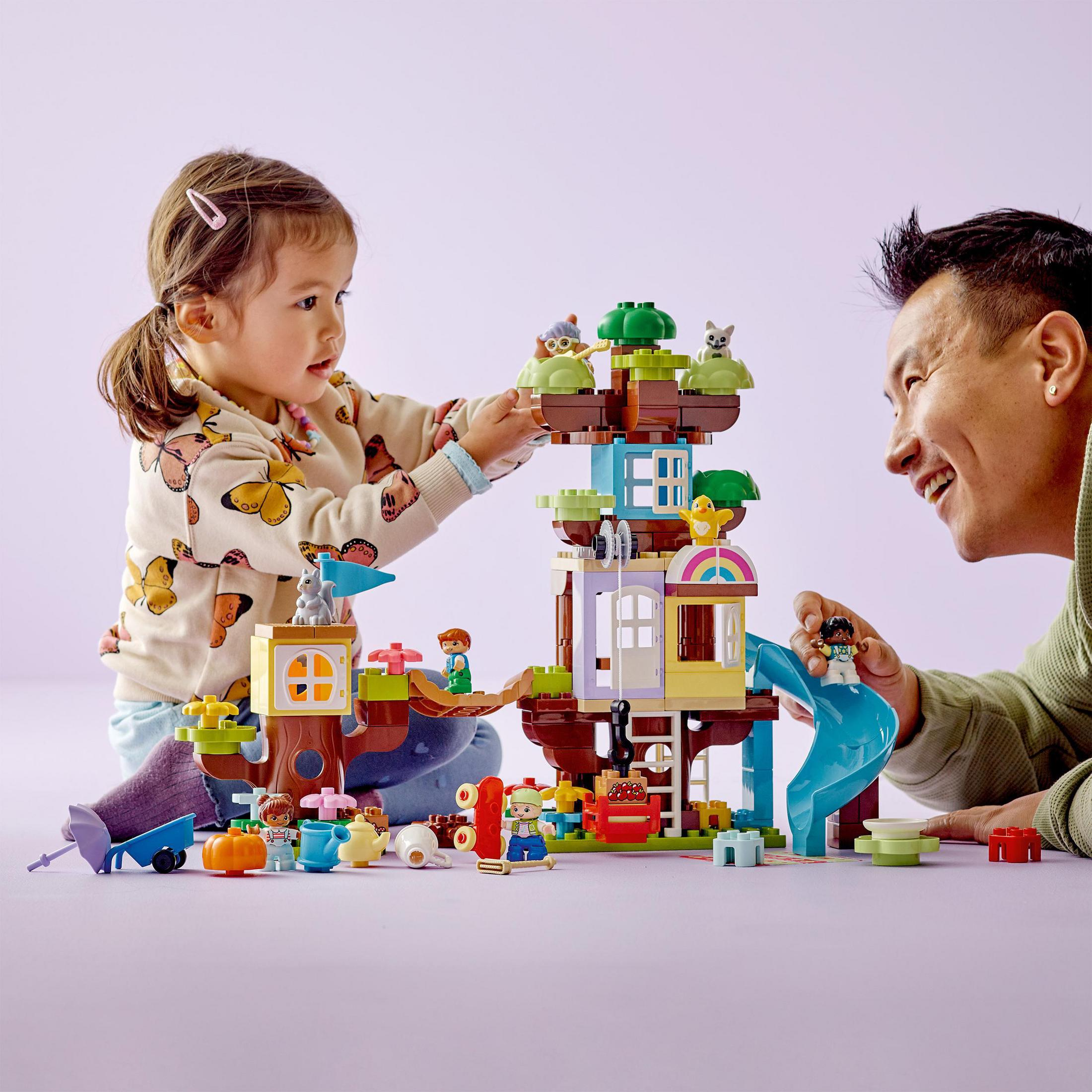 Lego Duplo Set. Kind und Erwachsener spielen mit Legosteinen. Lego-Haus mit Rutsche und Figuren.