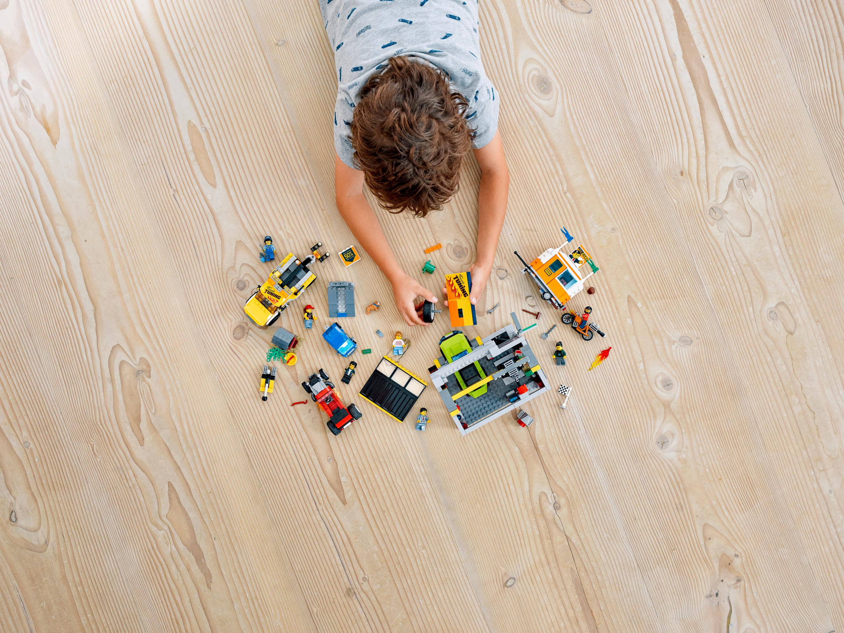 Dziecko bawiące się klockami LEGO na drewnianej podłodze. Różne zestawy LEGO rozrzucone.