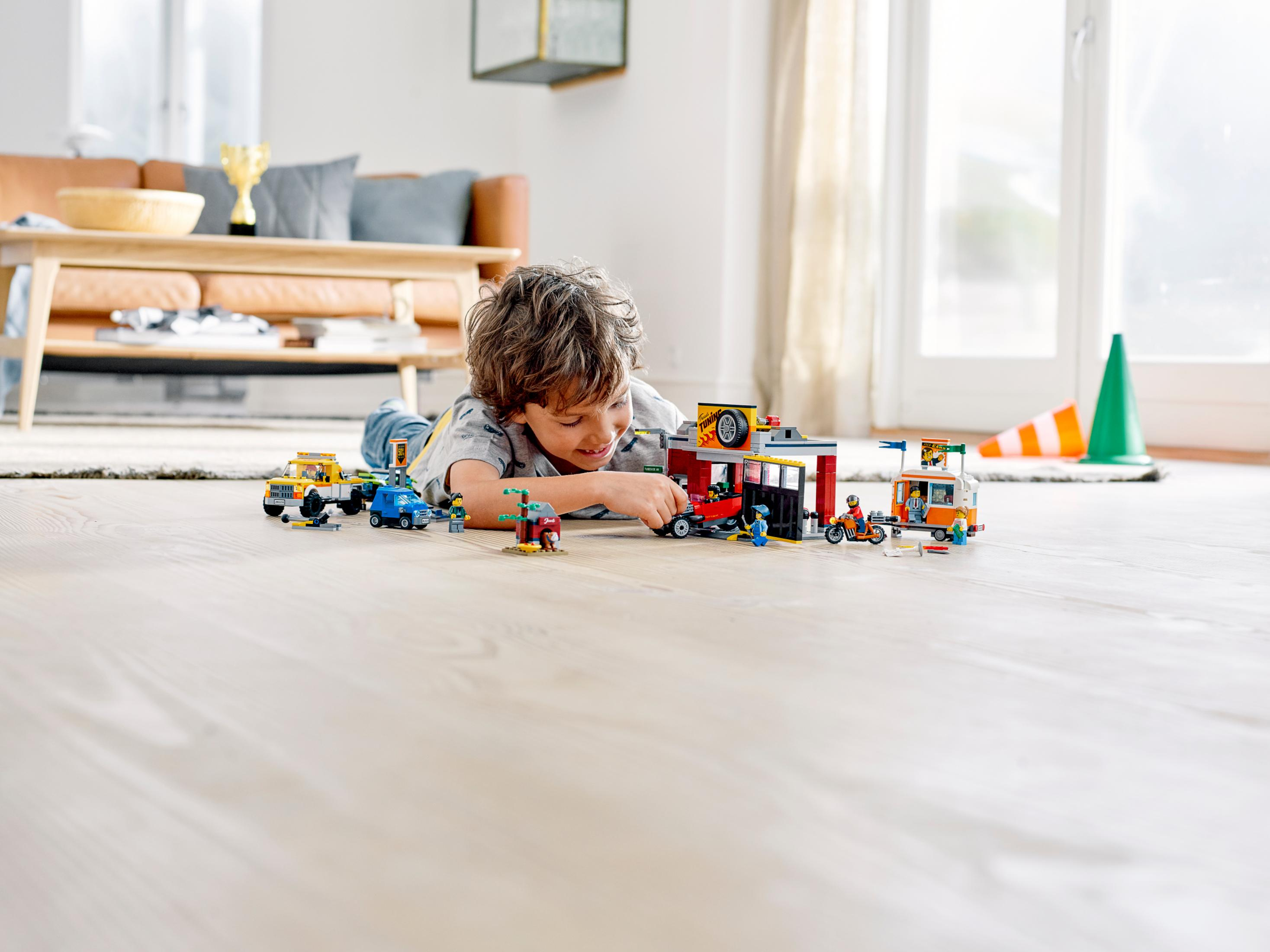 Dziecko leży na podłodze, bawiąc się zestawem Lego City z samochodami i budynkami.