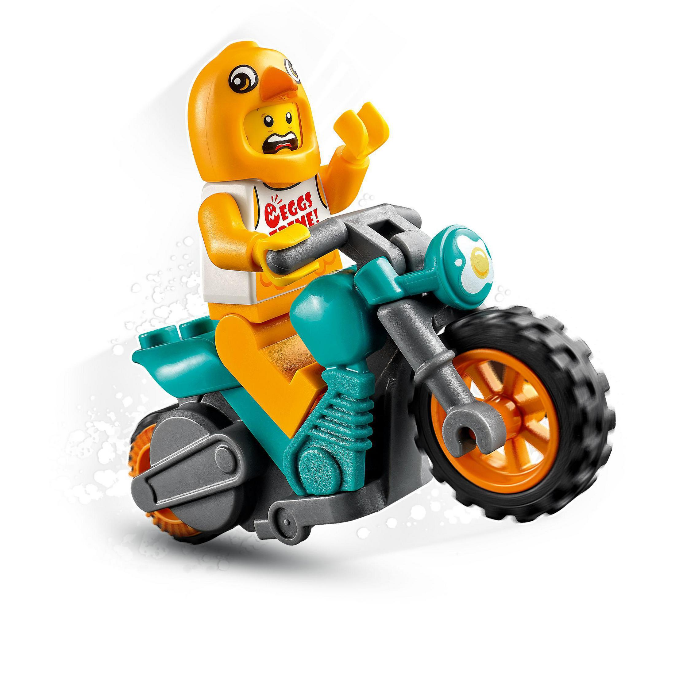 Eine Lego-Figur als Küken verkleidet, fährt auf einem teal- und orangefarbenen Motorrad, weißer Hintergrund.