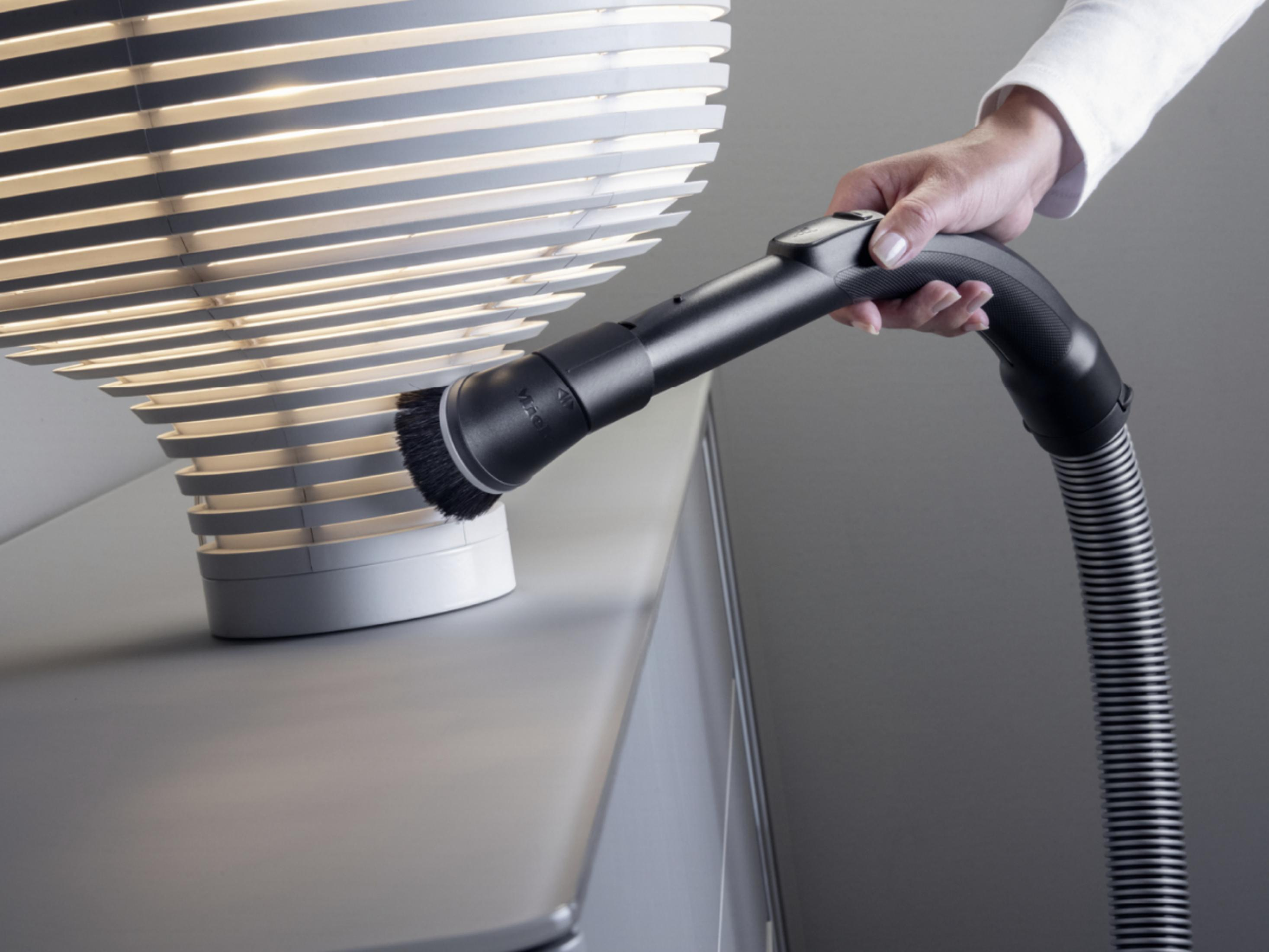 Eine Person reinigt eine Lampe mit einem Bürstenaufsatz an einem Staubsauger.