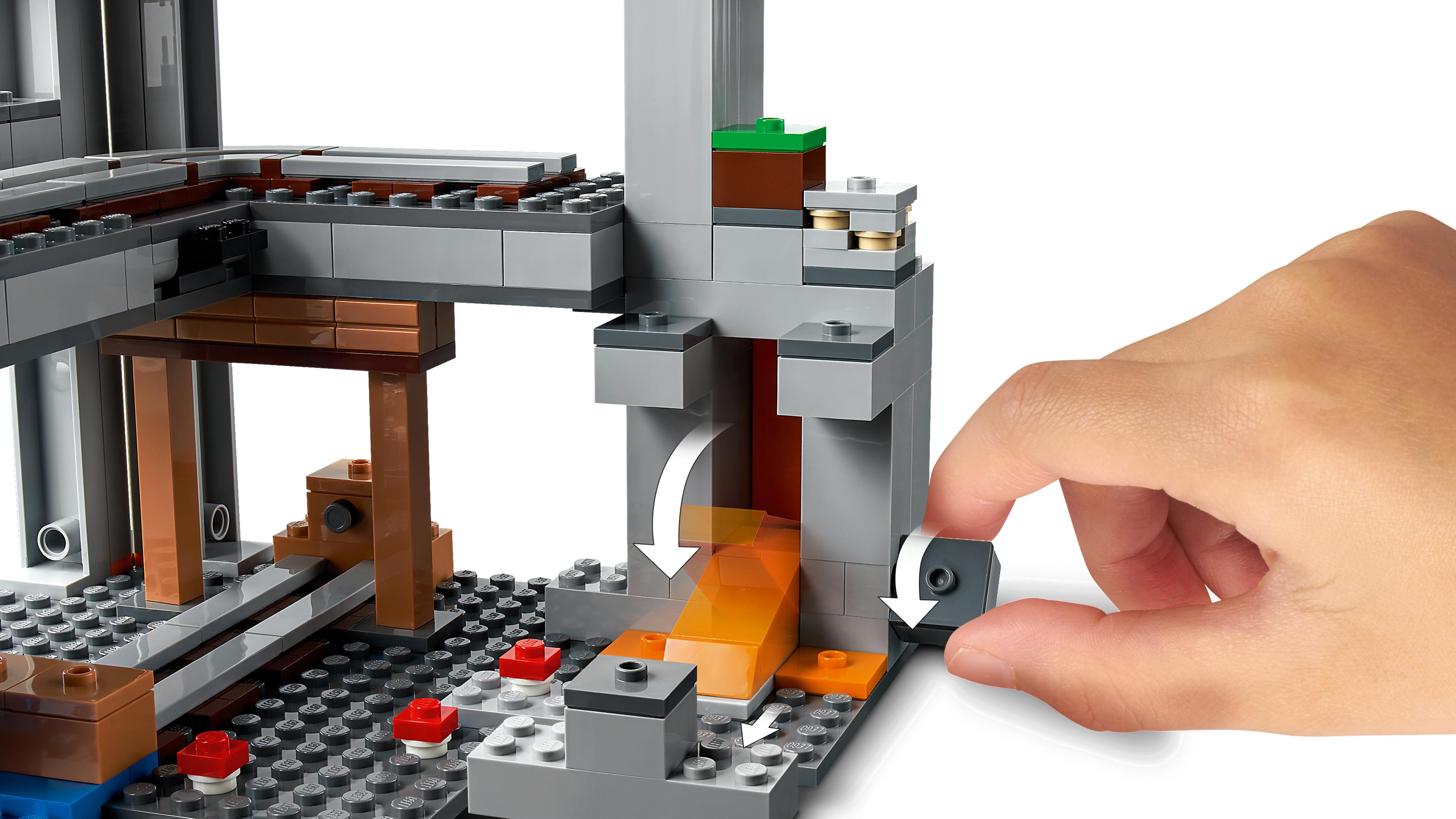 Eine Hand, die ein Lego Minecraft-Set anpasst. Die Szene zeigt eine Mine mit Lava und einer Strecke, sowie graue Blöcke.
