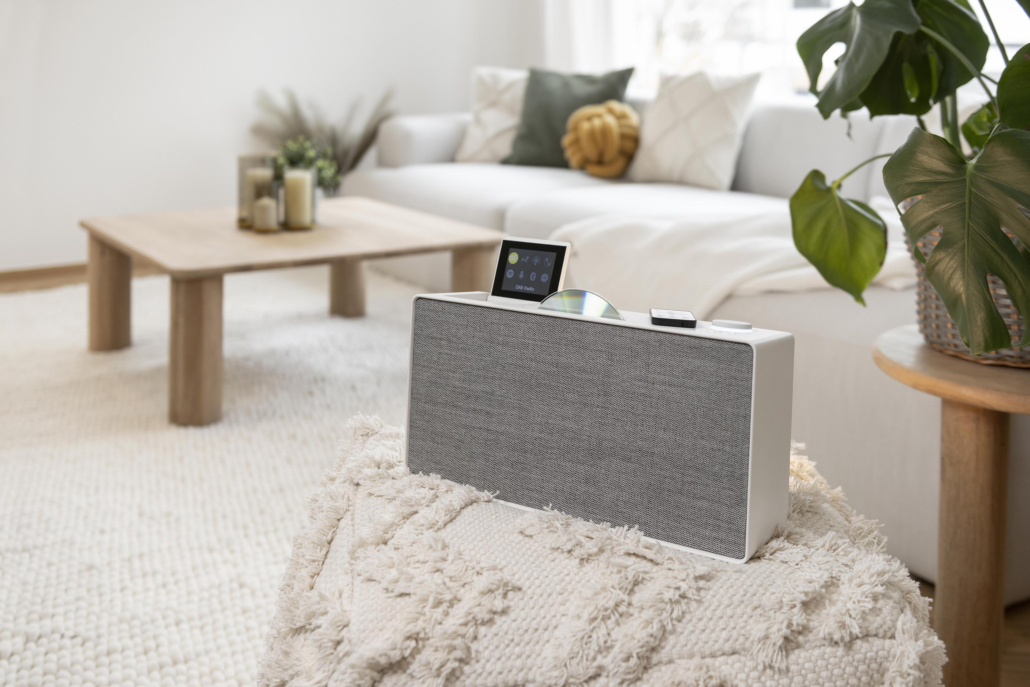 Biały głośnik z płytą CD na górze, na wzorzystym dywanie, w salonie.