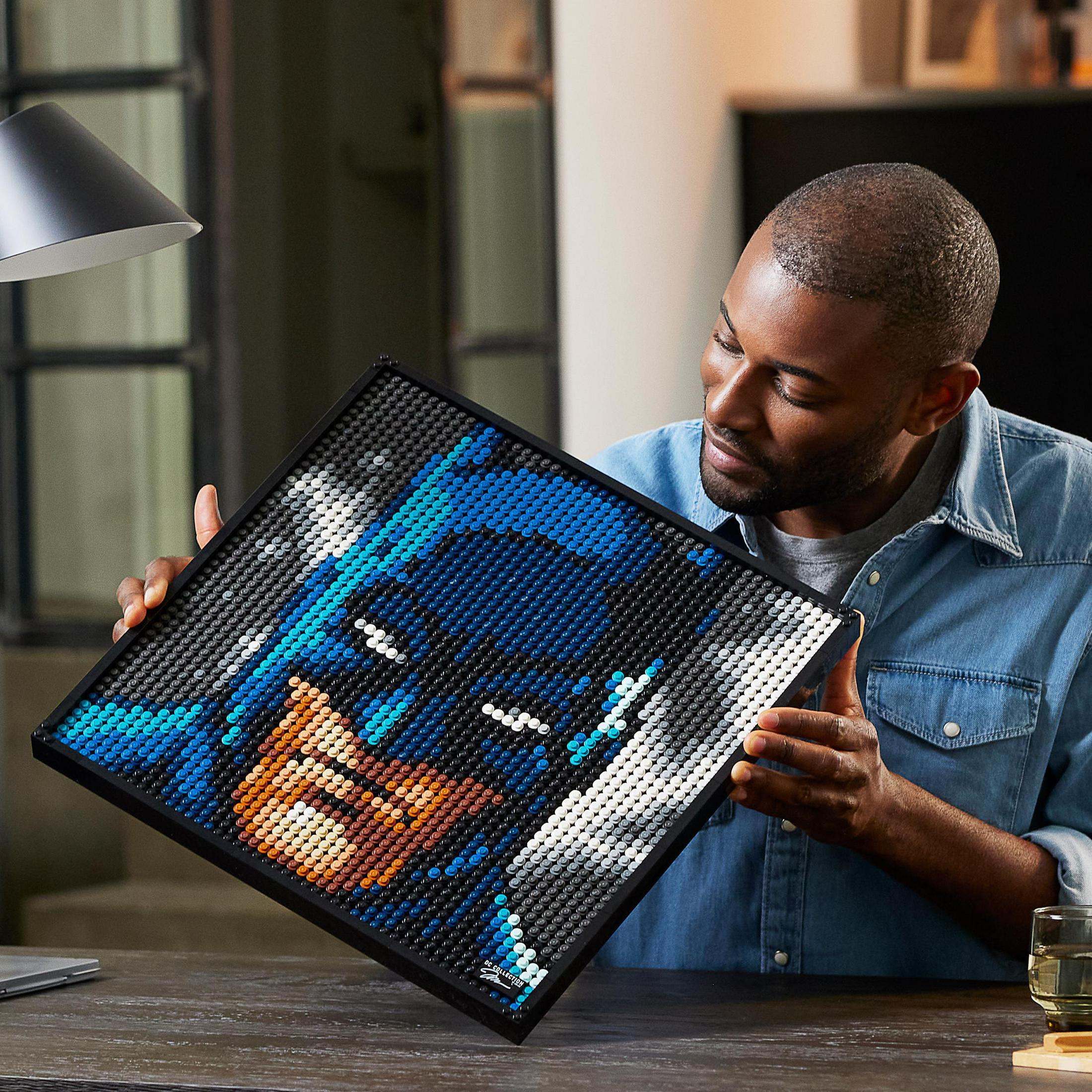 Mężczyzna trzyma zestaw Lego z Batmanem, patrząc na niego. Zestaw jest na stole.