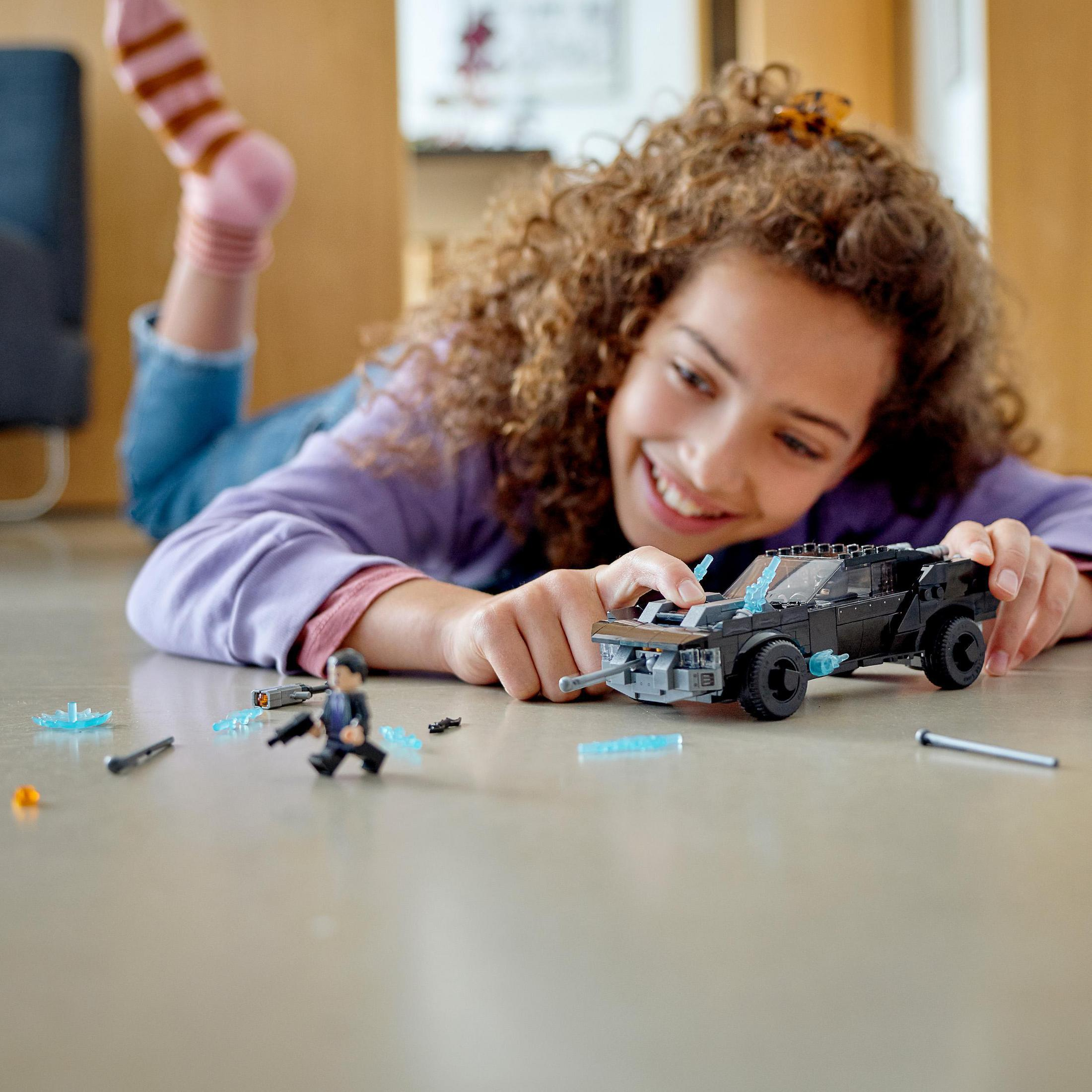 Ein Mädchen spielt mit einem Lego Batmobil-Set. Auf dem Boden liegen Lego-Figuren.