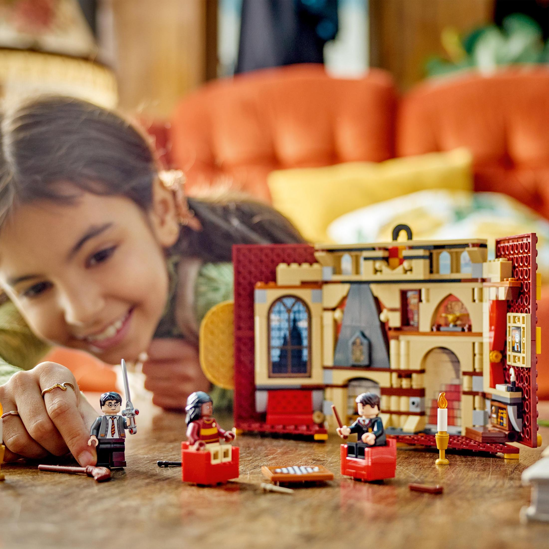 Mädchen spielt mit Lego Harry Potter Set. Figuren und Gebäude auf dem Tisch. Lächelt. Verschwommener Hintergrund.