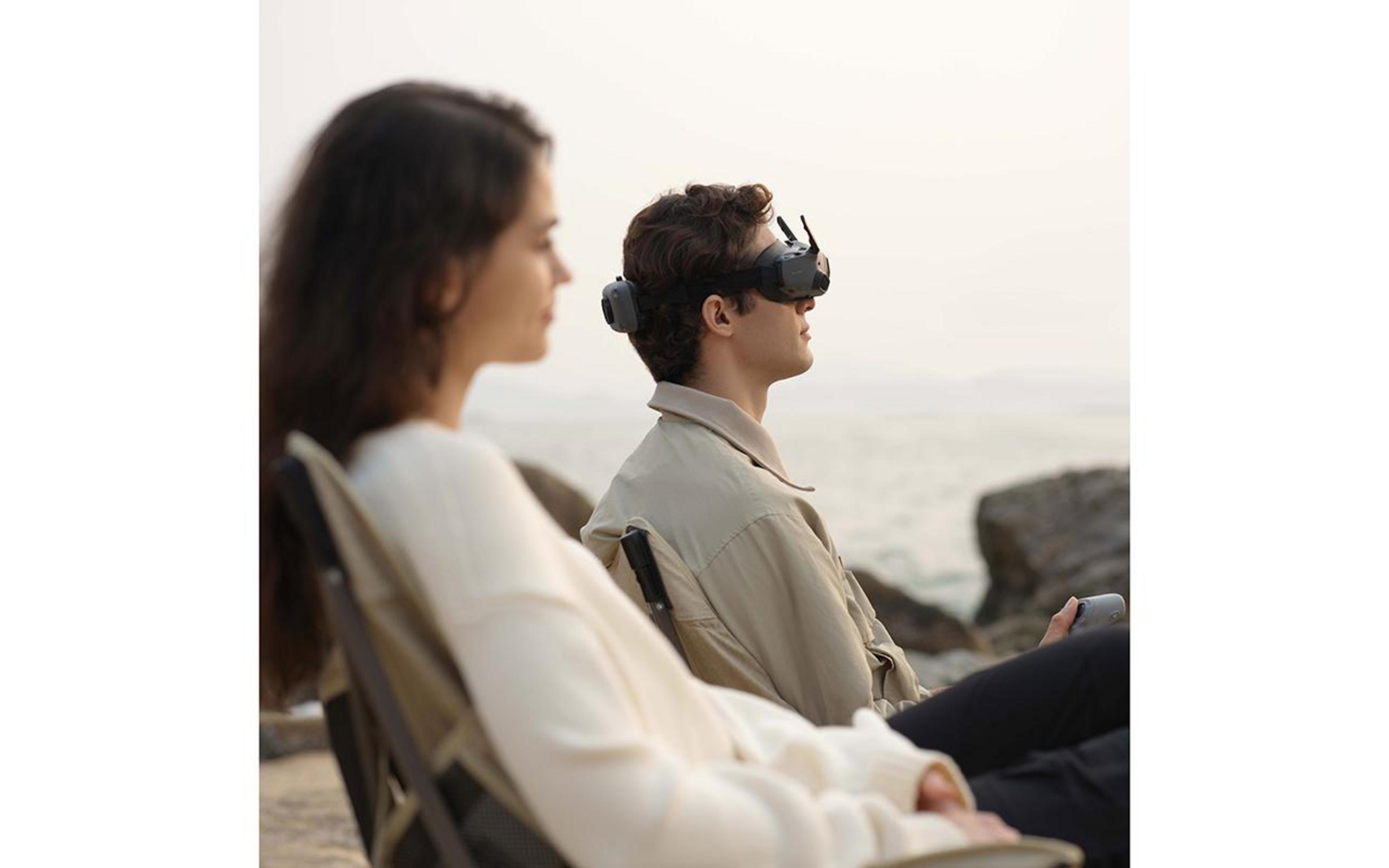 Ein Mann mit VR-Headset sitzt neben einer Frau. Sie sind in der Nähe des Wassers.