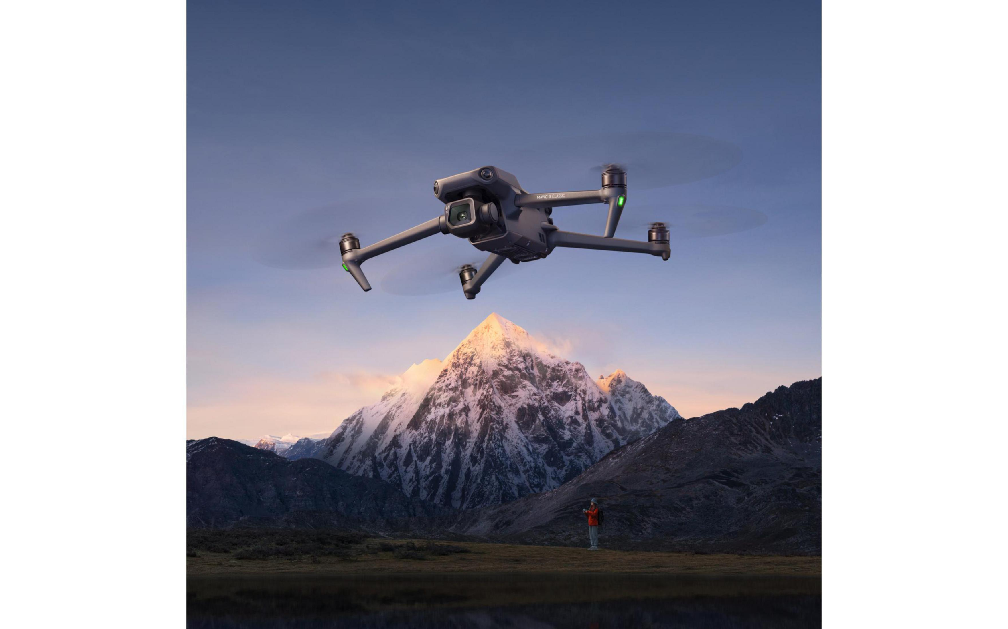 Eine Drohne im Flug über einem Bergmassiv. In der Ferne ist eine Person zu sehen.