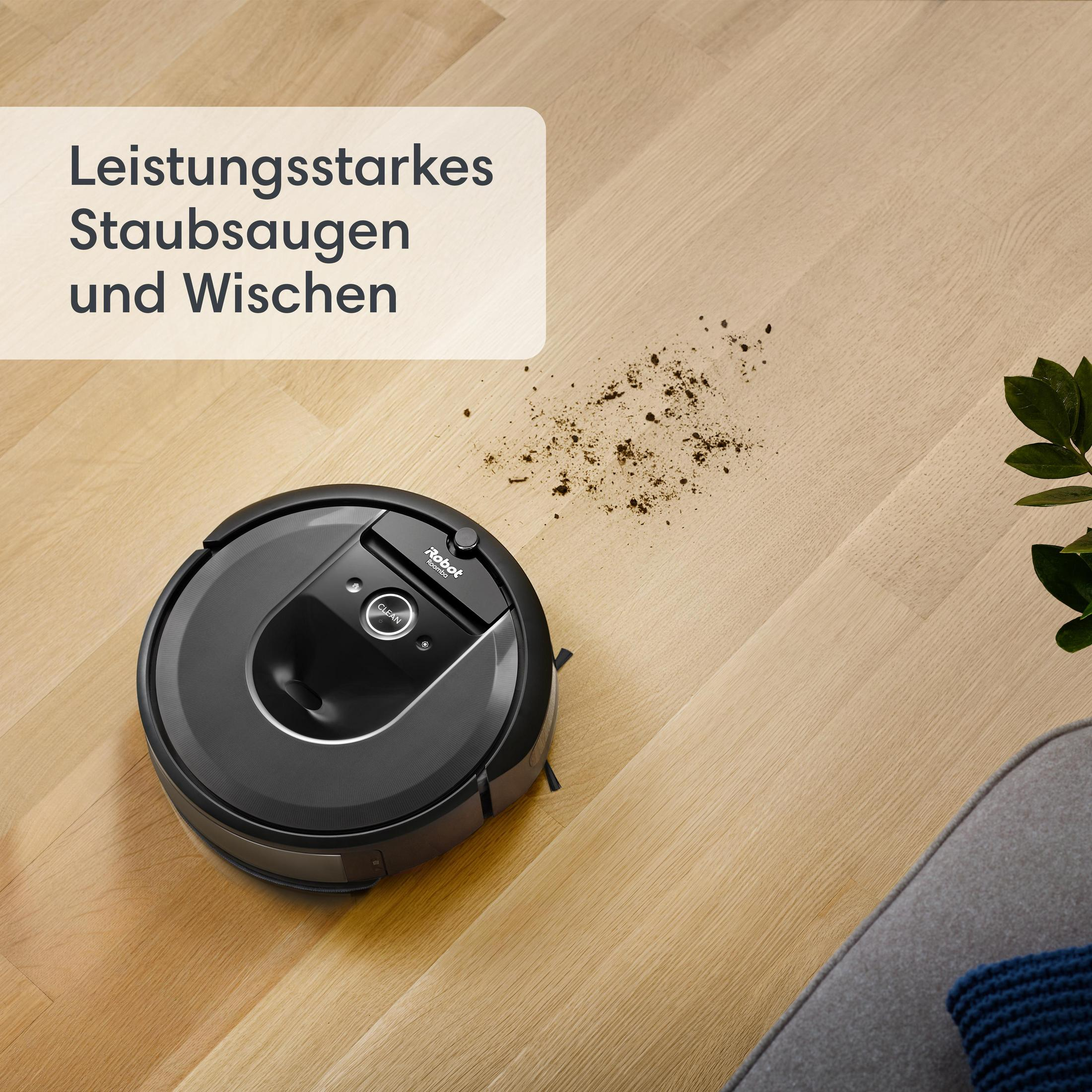 A black robot vacuum cleaner on a wooden floor with debris.