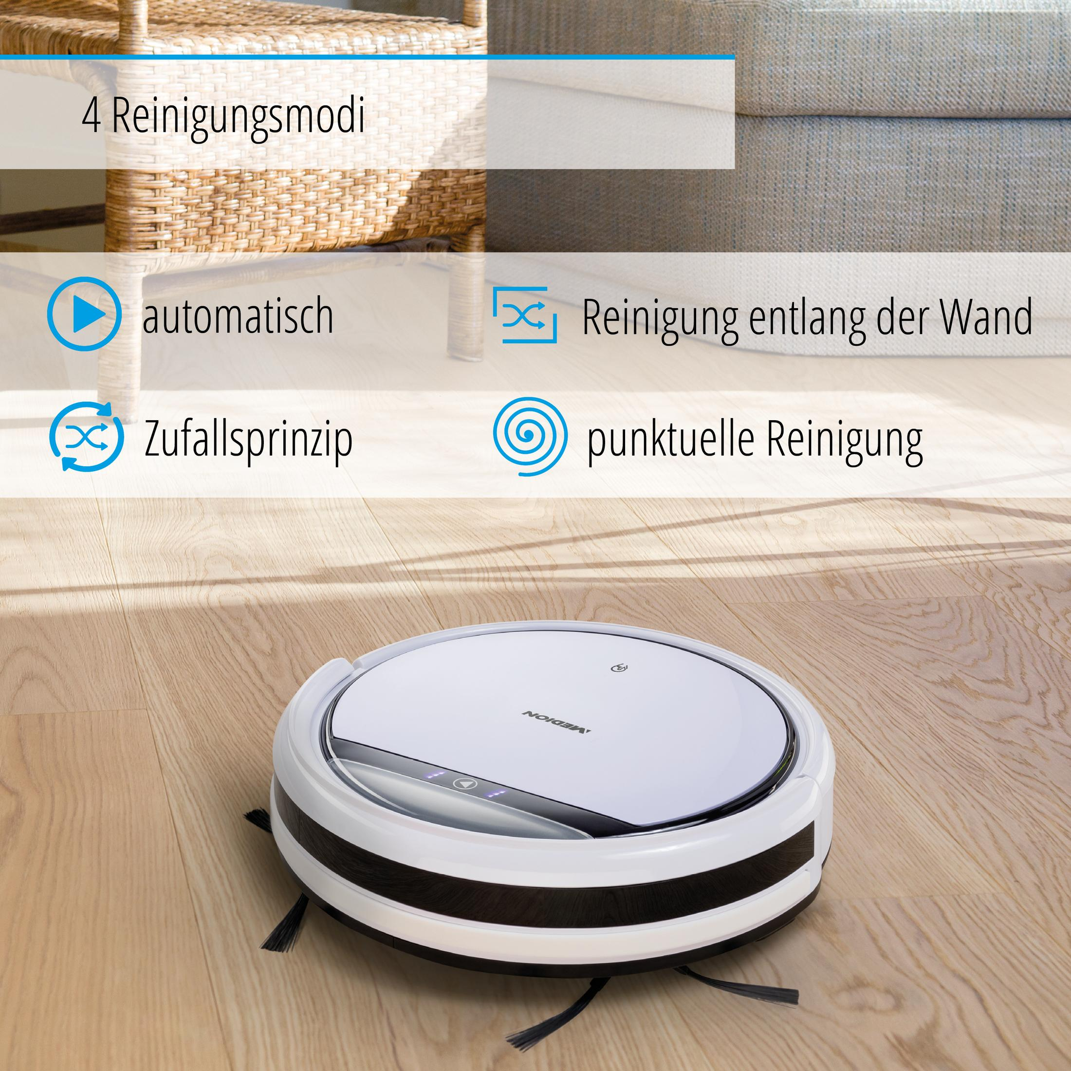 Aspirapolvere robot bianco su pavimento in legno. Ha un paraurti nero ed è vicino a un divano.