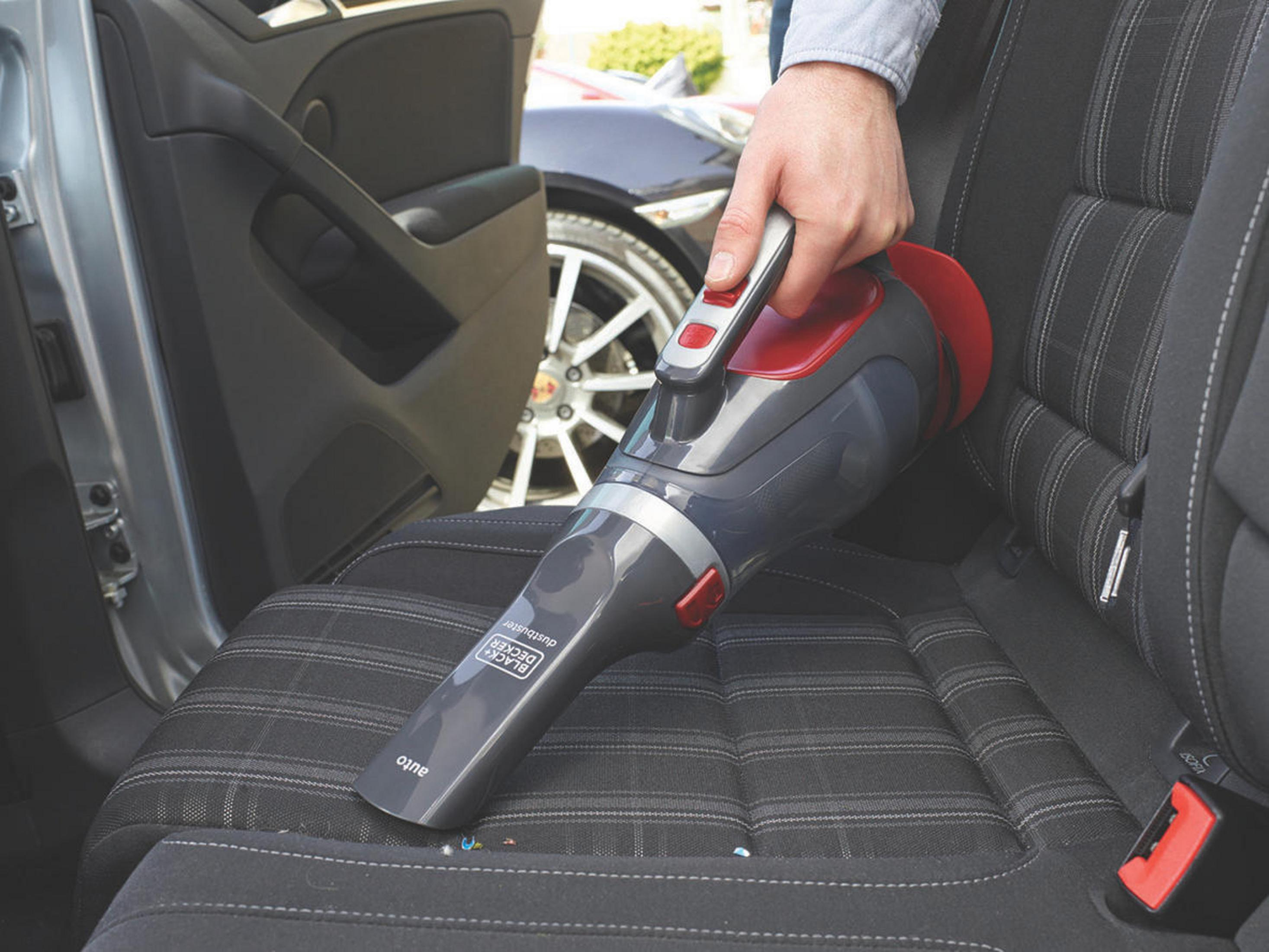 Ręka używająca szaro-czerwonego odkurzacza ręcznego do czyszczenia siedzenia samochodu.