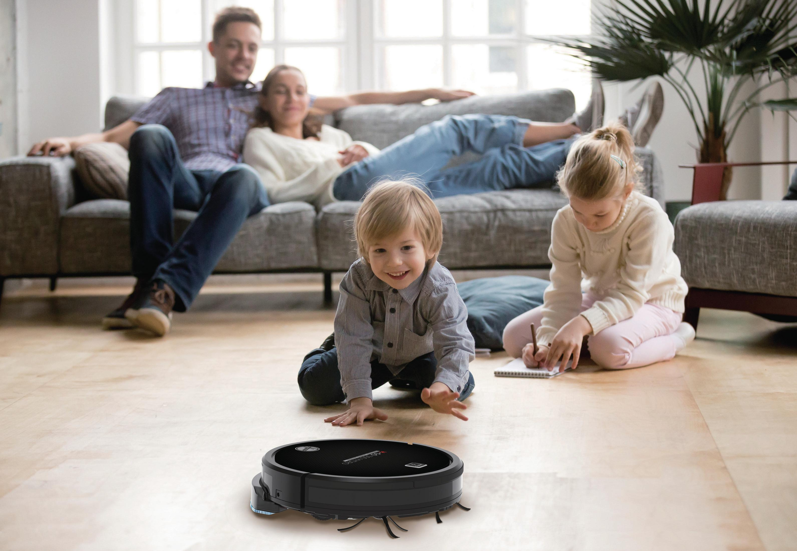 Ein schwarzer Roboter-Staubsauger auf einem Boden mit einer Familie im Hintergrund, die lächelt.