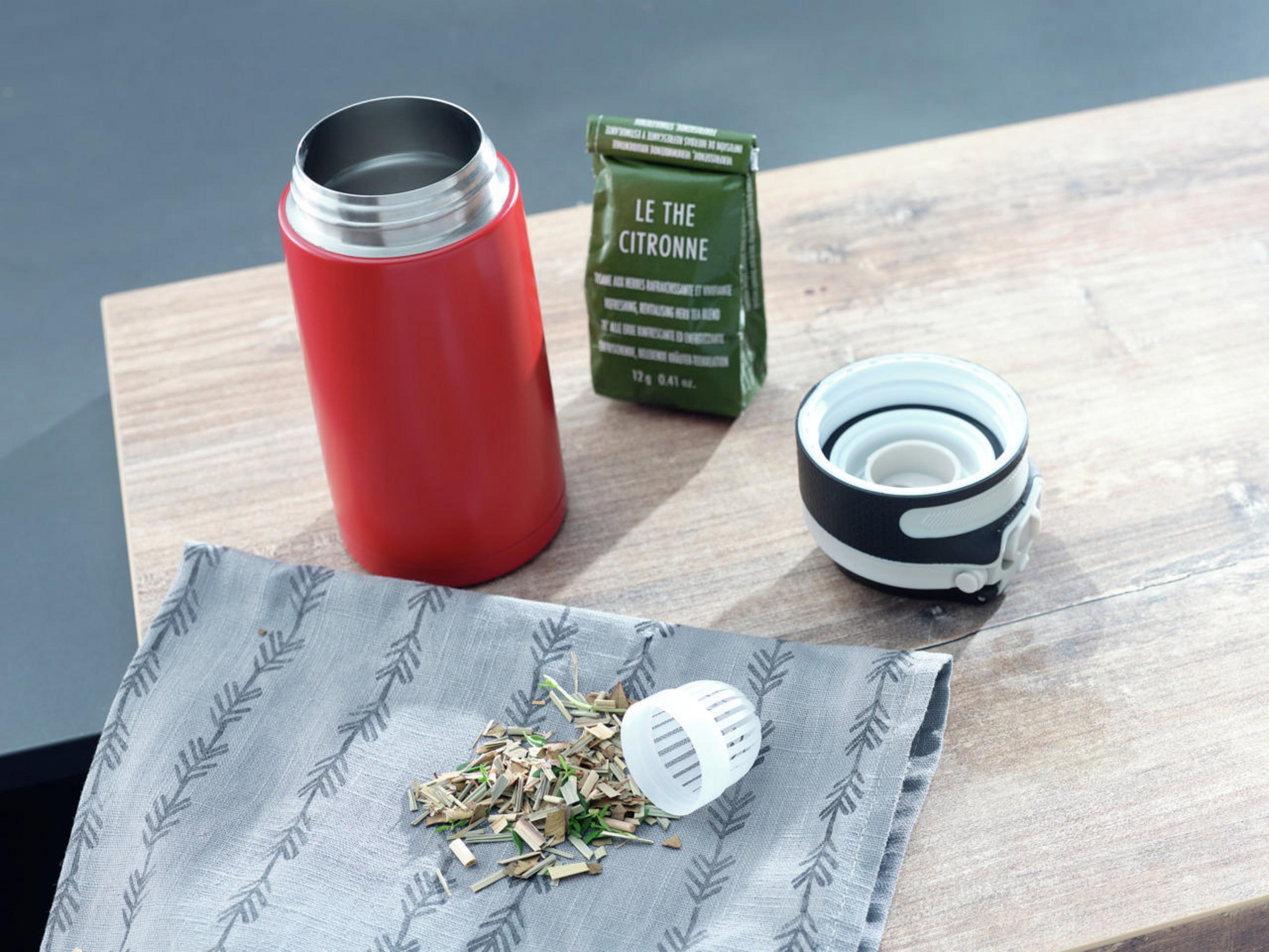 Eine rote isolierte Wasserflasche, ein Teebeutel und lose Teeblätter auf einem Holztisch.