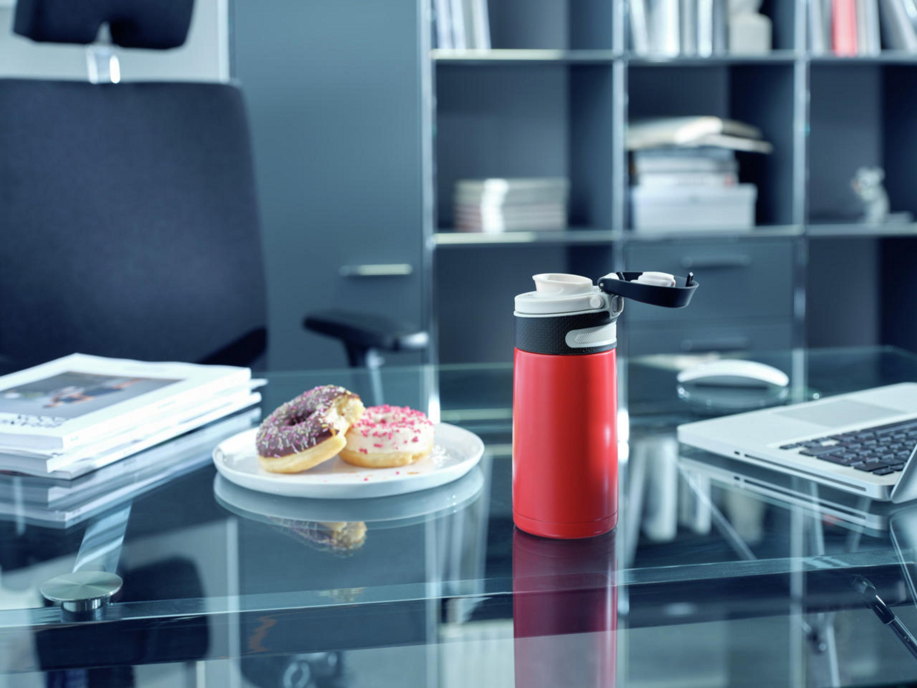 Rote Wasserflasche und Donuts auf Glastisch. Büroumgebung. Schwarzer Bürostuhl im Hintergrund.
