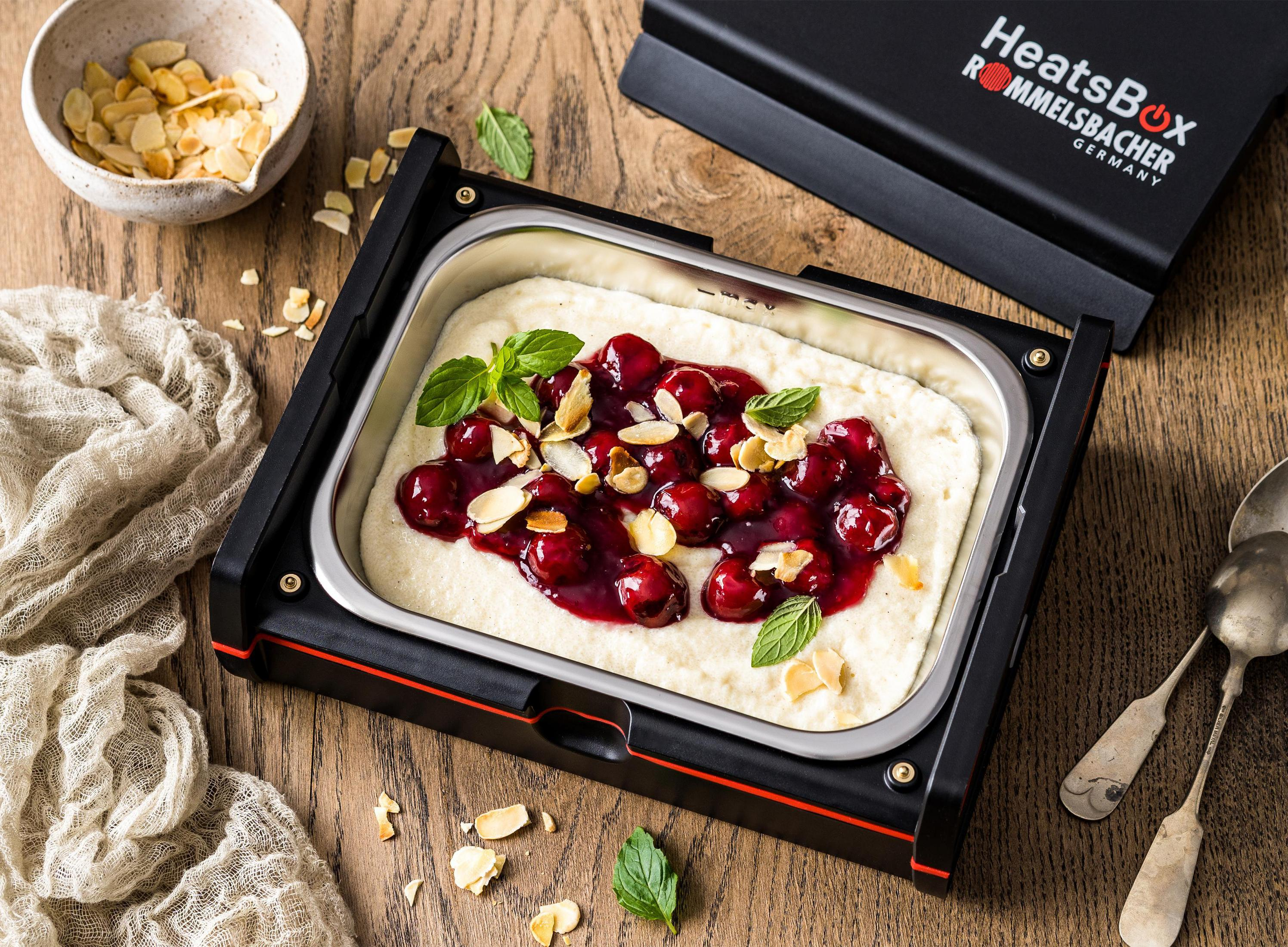 Speisenwärmer mit Kirschbelag und Mandeln. Minzblätter am Rand. Schwarze HeatsBox.