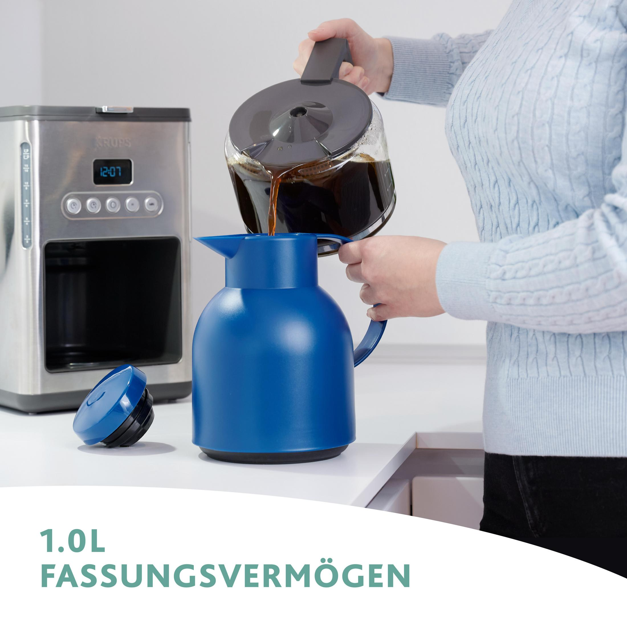 Frau gießt Kaffee aus einer Glaskaraffe in eine blaue Thermoskanne. Eine Kaffeemaschine steht links.