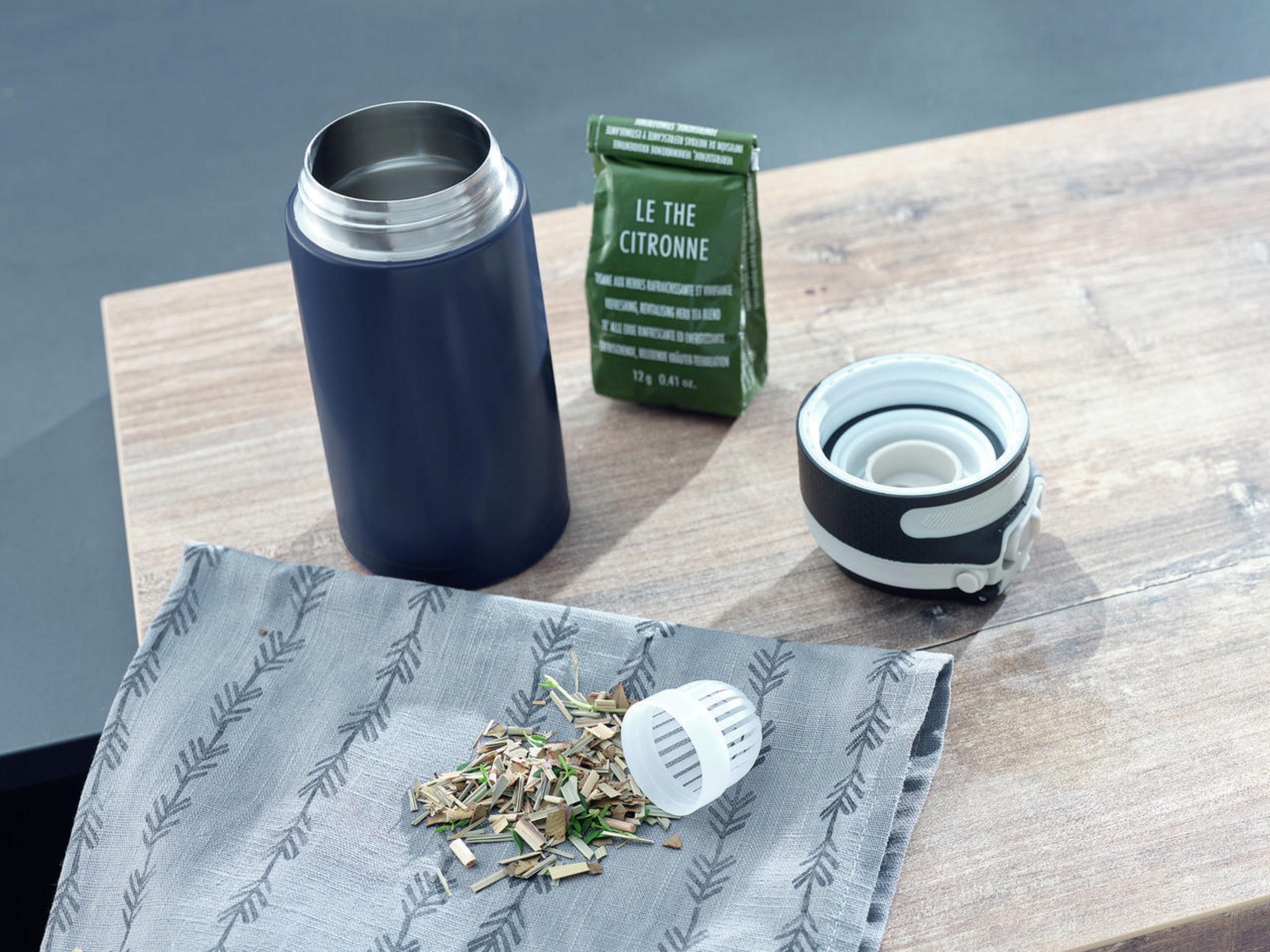 Eine marineblaue Thermosflasche mit Teeblättern und einem Teebeutel auf einem Holztisch.