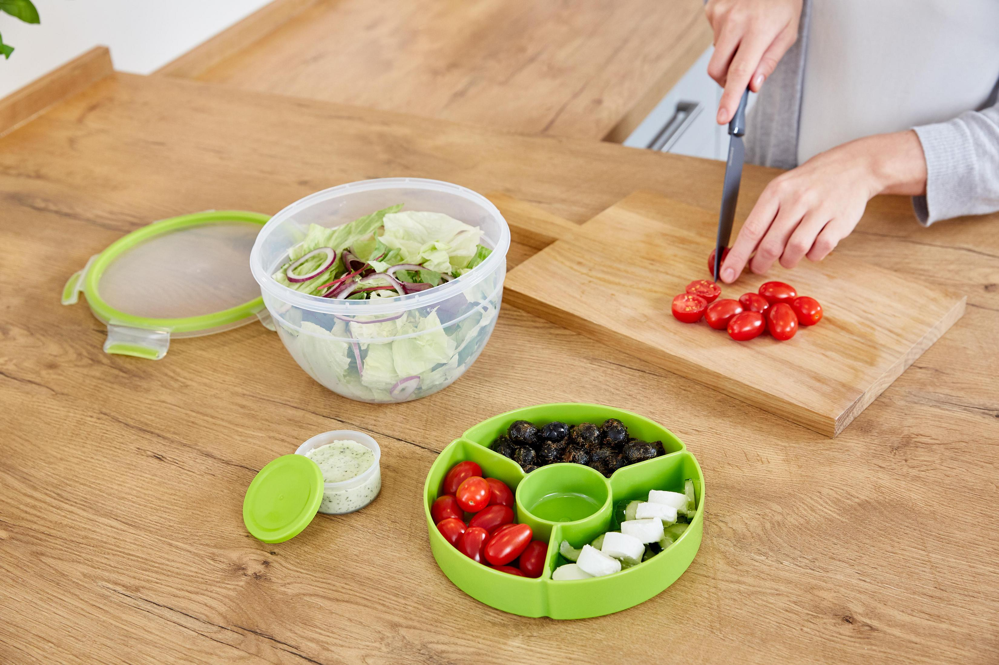 Eine Person schneidet Kirschtomaten auf einem Holzbrett neben Salat und einer Servierschale.