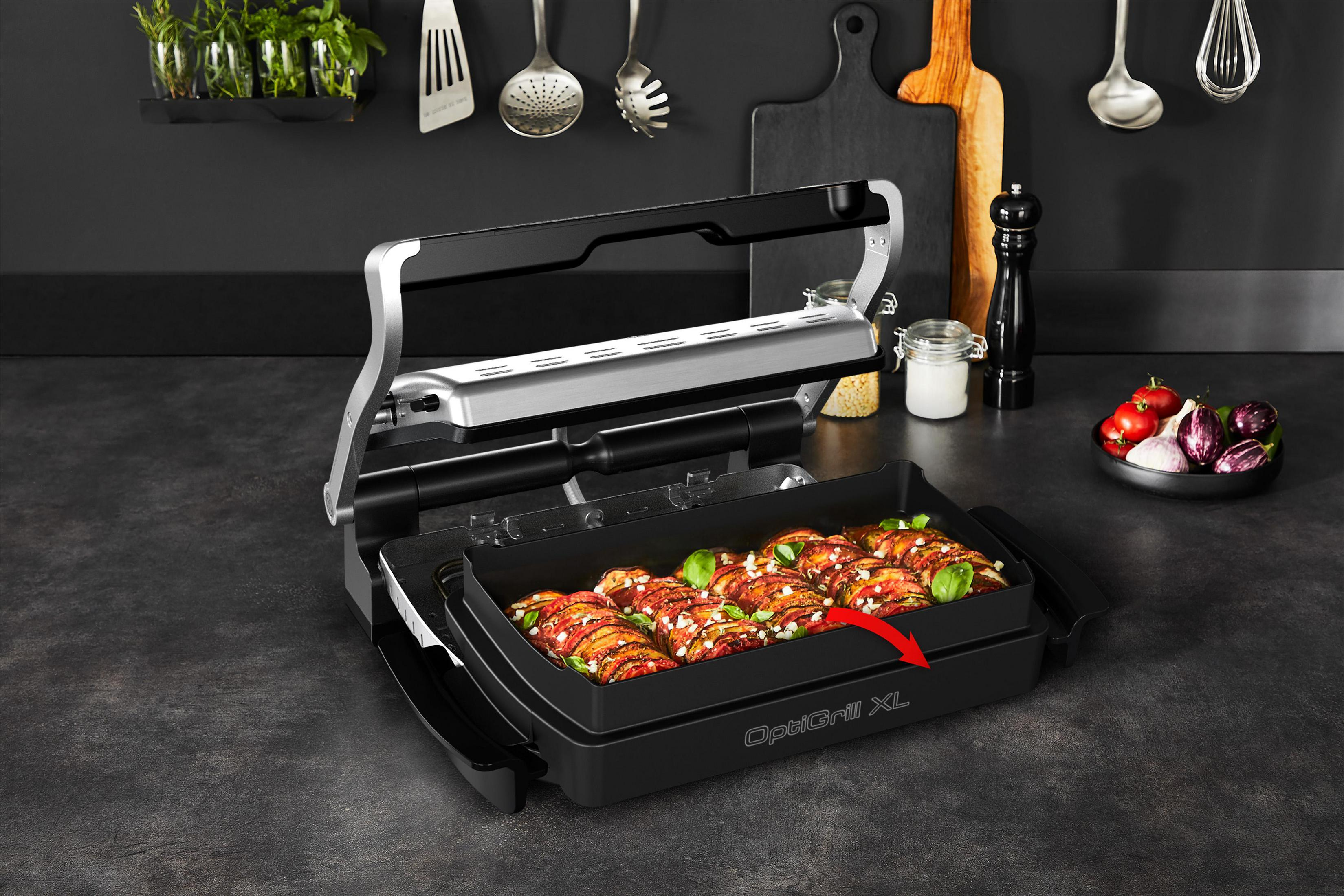 Grill with food inside and vegetables on counter, kitchen setting, black and silver.