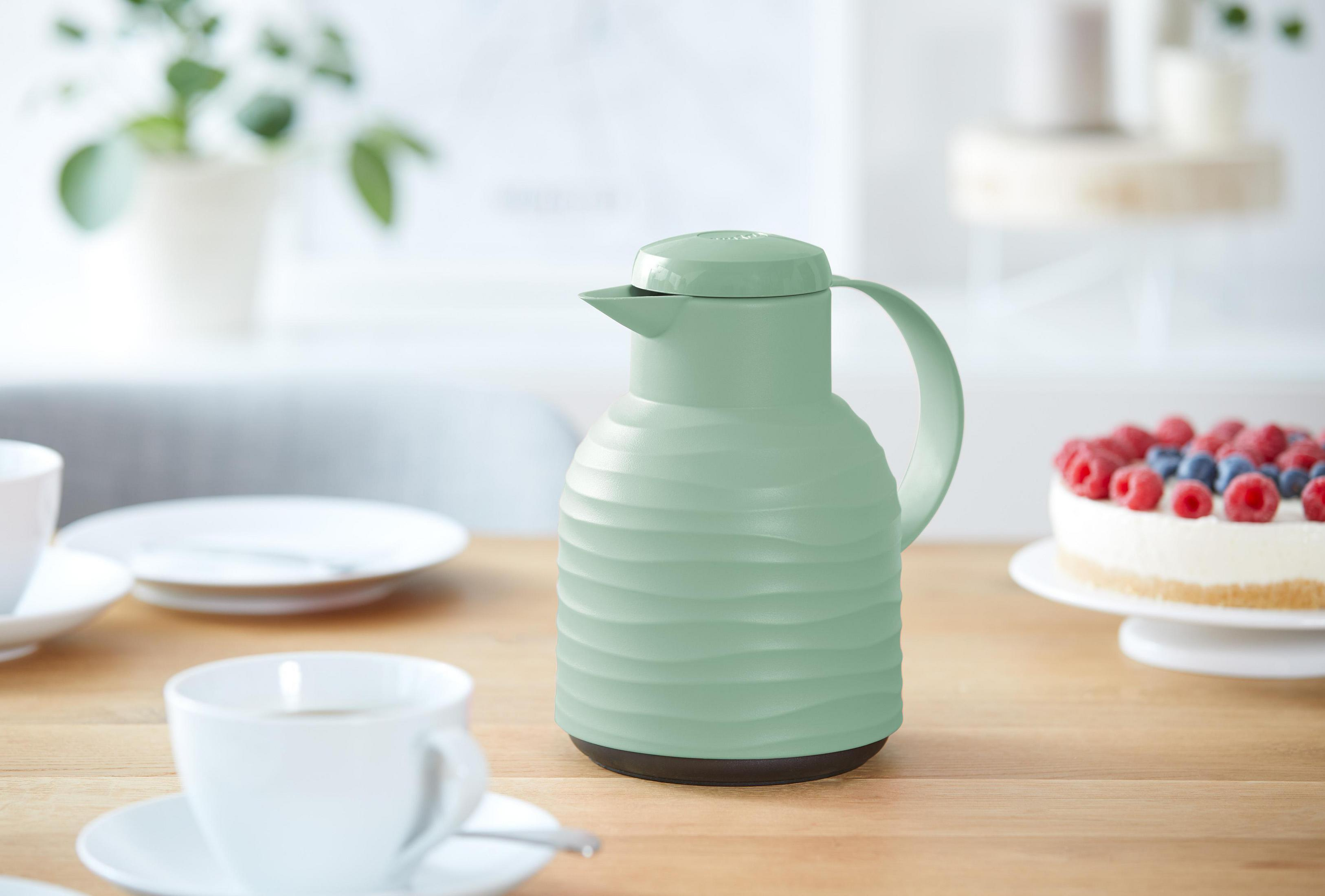 Eine grüne, gerippte Thermoskanne und eine weiße Tasse und Untertasse stehen auf einem Holztisch.