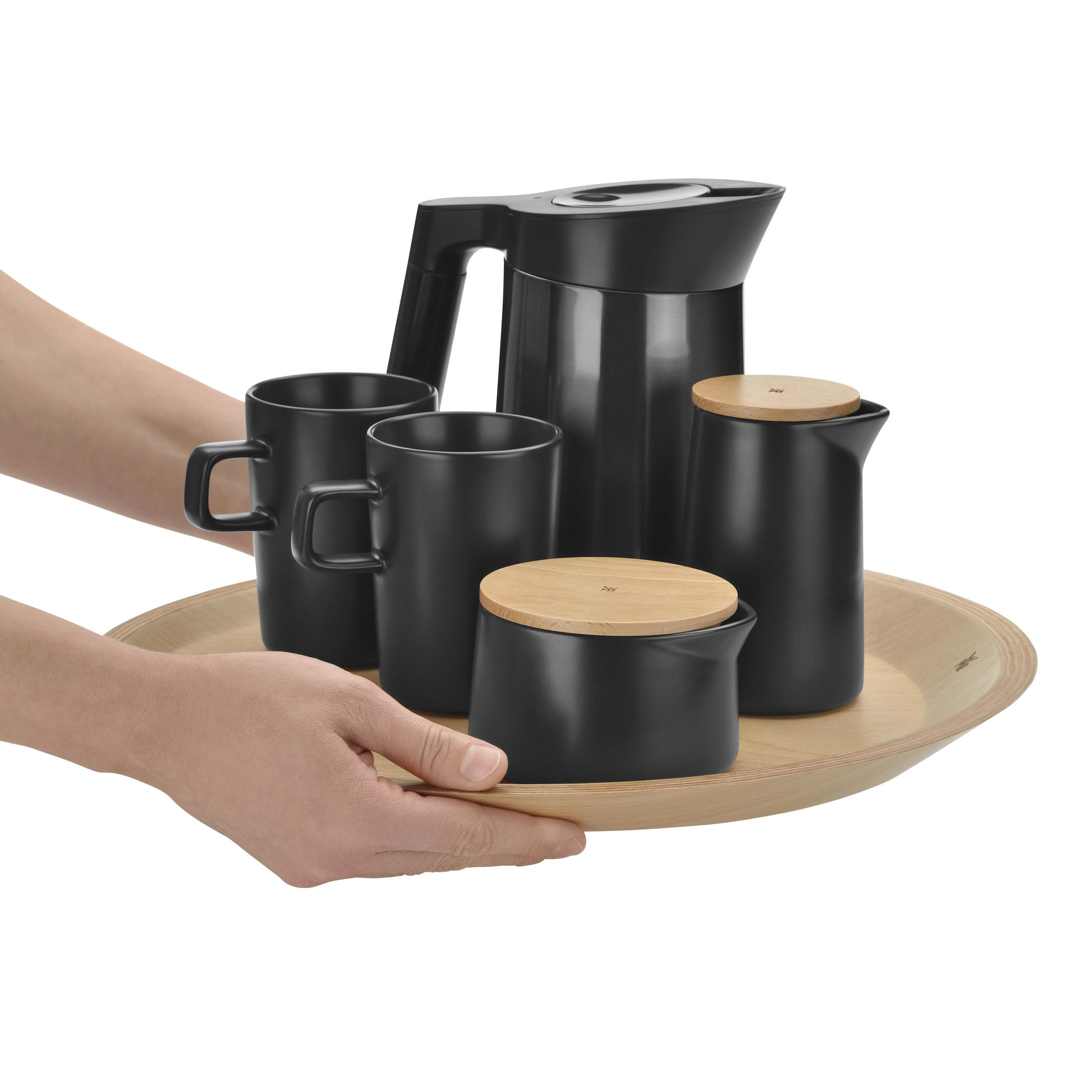 Set aus schwarzen Tassen, Krug und einem Holztablett, das von Händen gehalten wird.