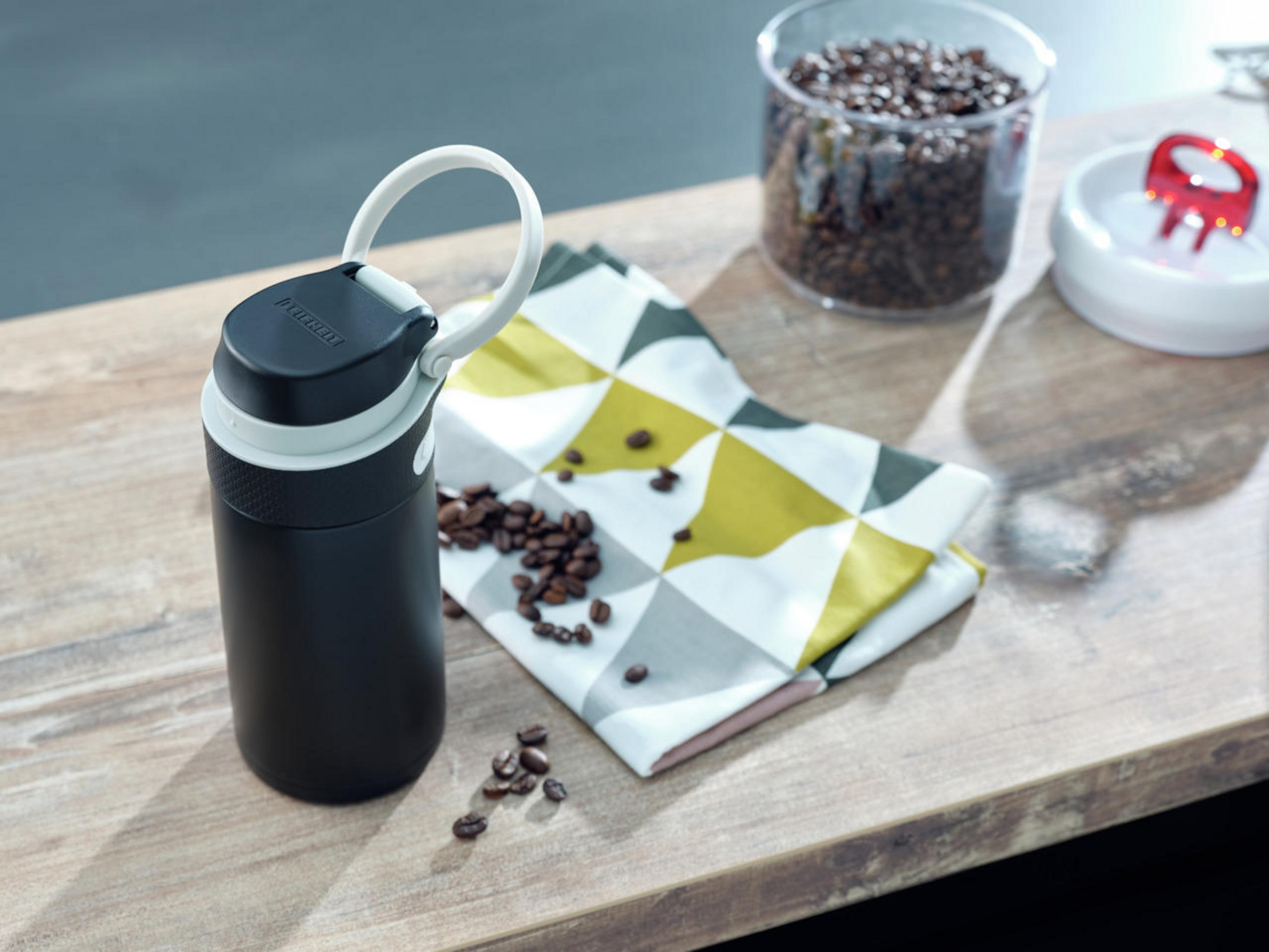 Schwarz-weiße Flasche und Kaffeebohnen auf Holzoberfläche.