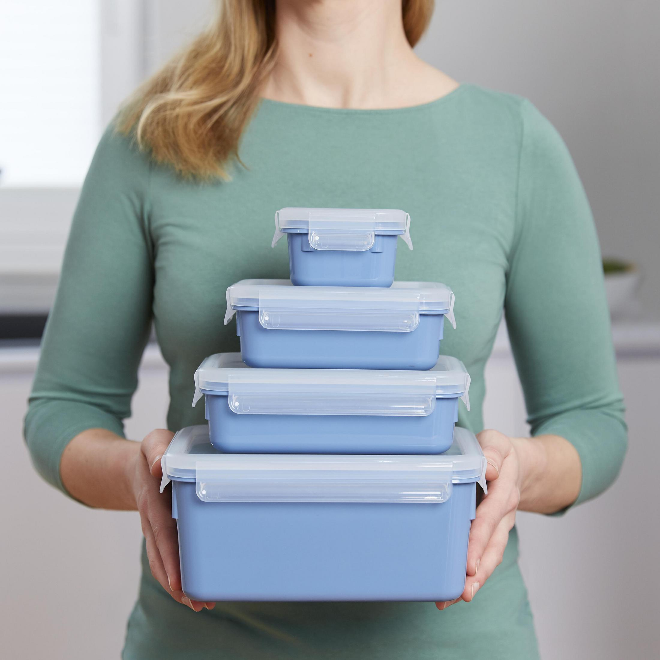 Eine Frau hält einen Stapel von vier blauen Lebensmittellagern mit weißen Deckeln. Sauber, organisiert.