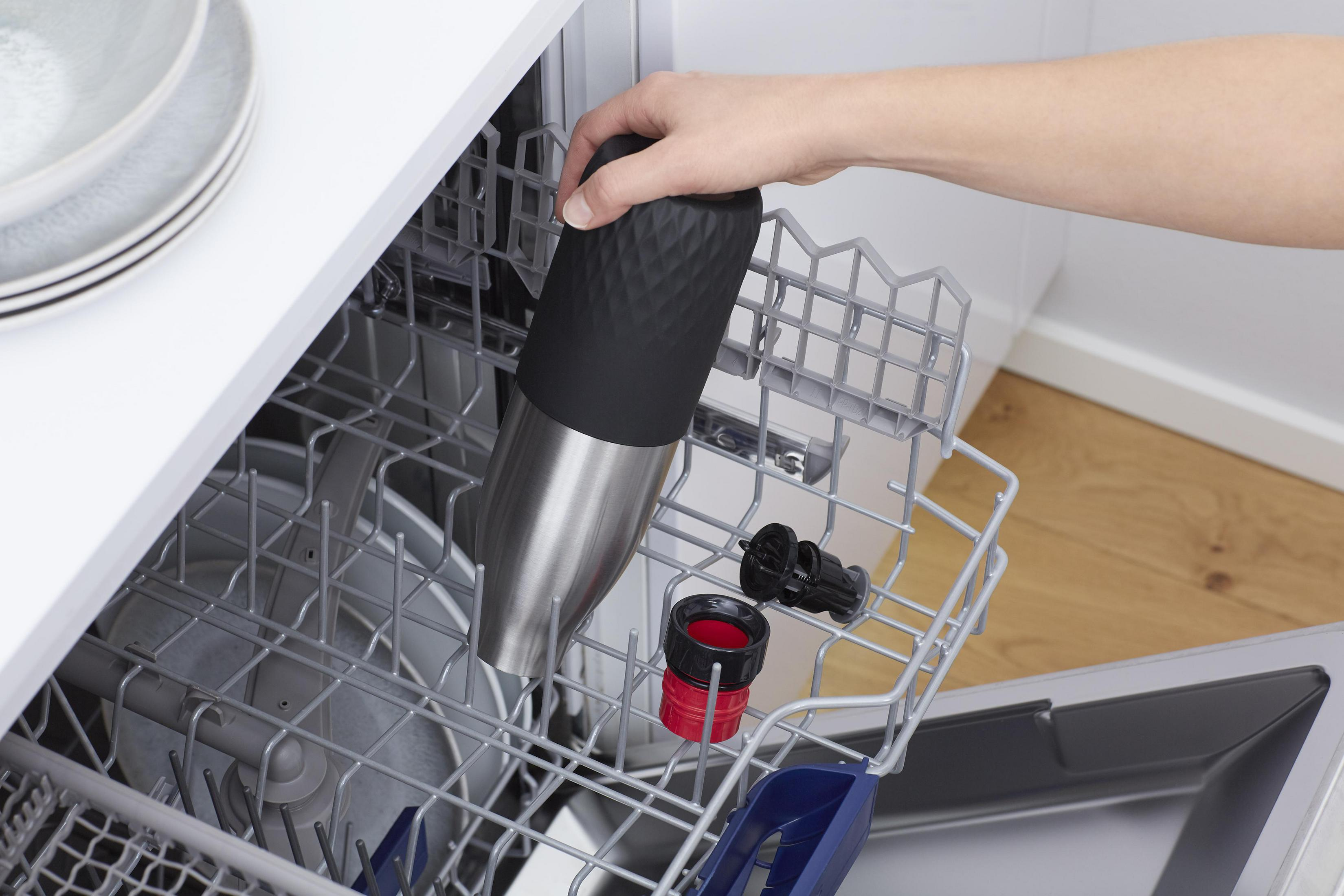 Eine Hand legt eine schwarze Wasserflasche in einen Geschirrspüler.