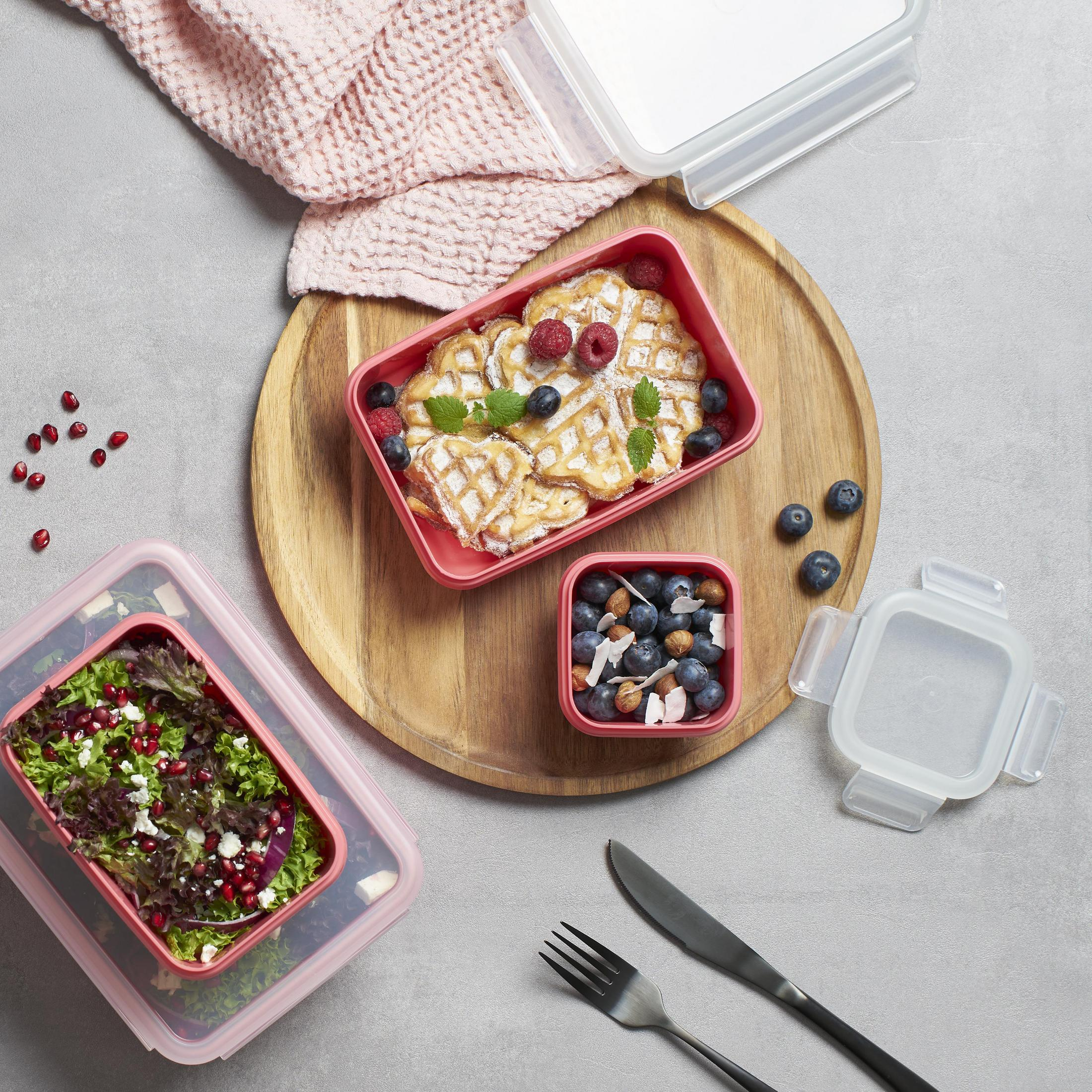 Lebensmittelbehälter auf einem Holzbrett. Waffeln, Salat und ein Snack mit Beeren und Nüssen.