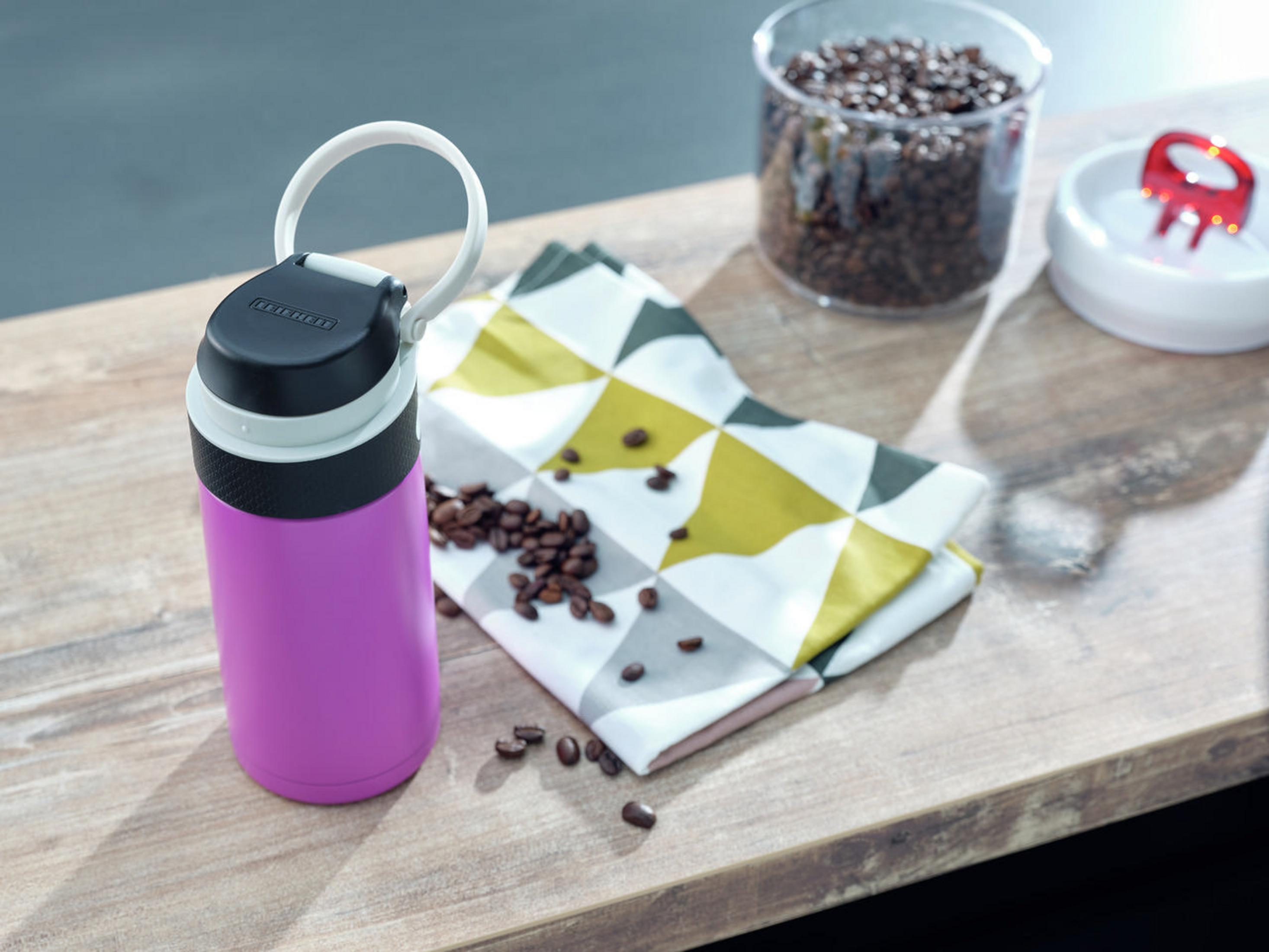 Rosa-schwarze Isolierflasche, Kaffeebohnen, Serviette und Glasbehälter auf Holzoberfläche.