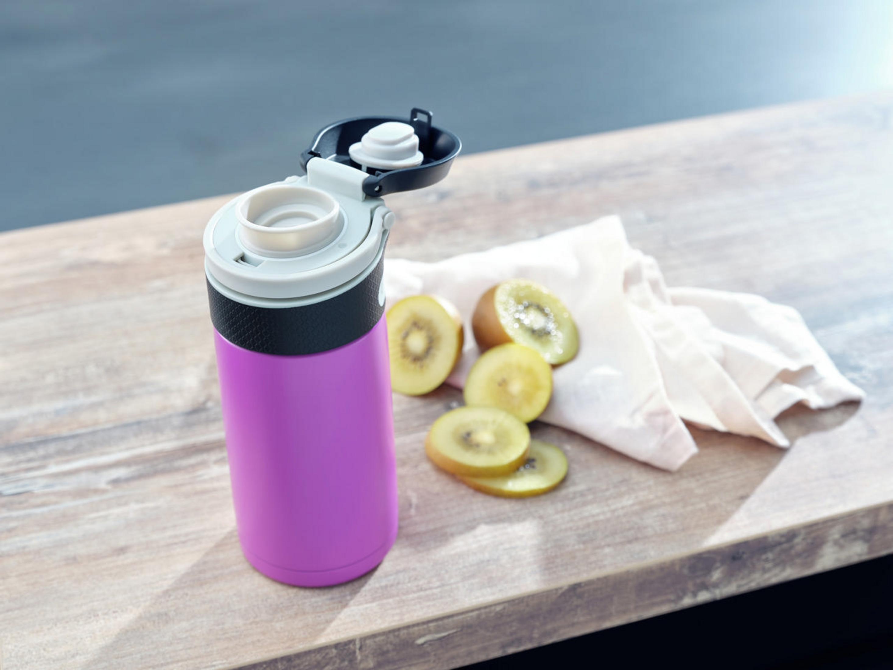 Eine lila Wasserflasche, Kiwischeiben und ein Tuch auf einer Holzoberfläche.