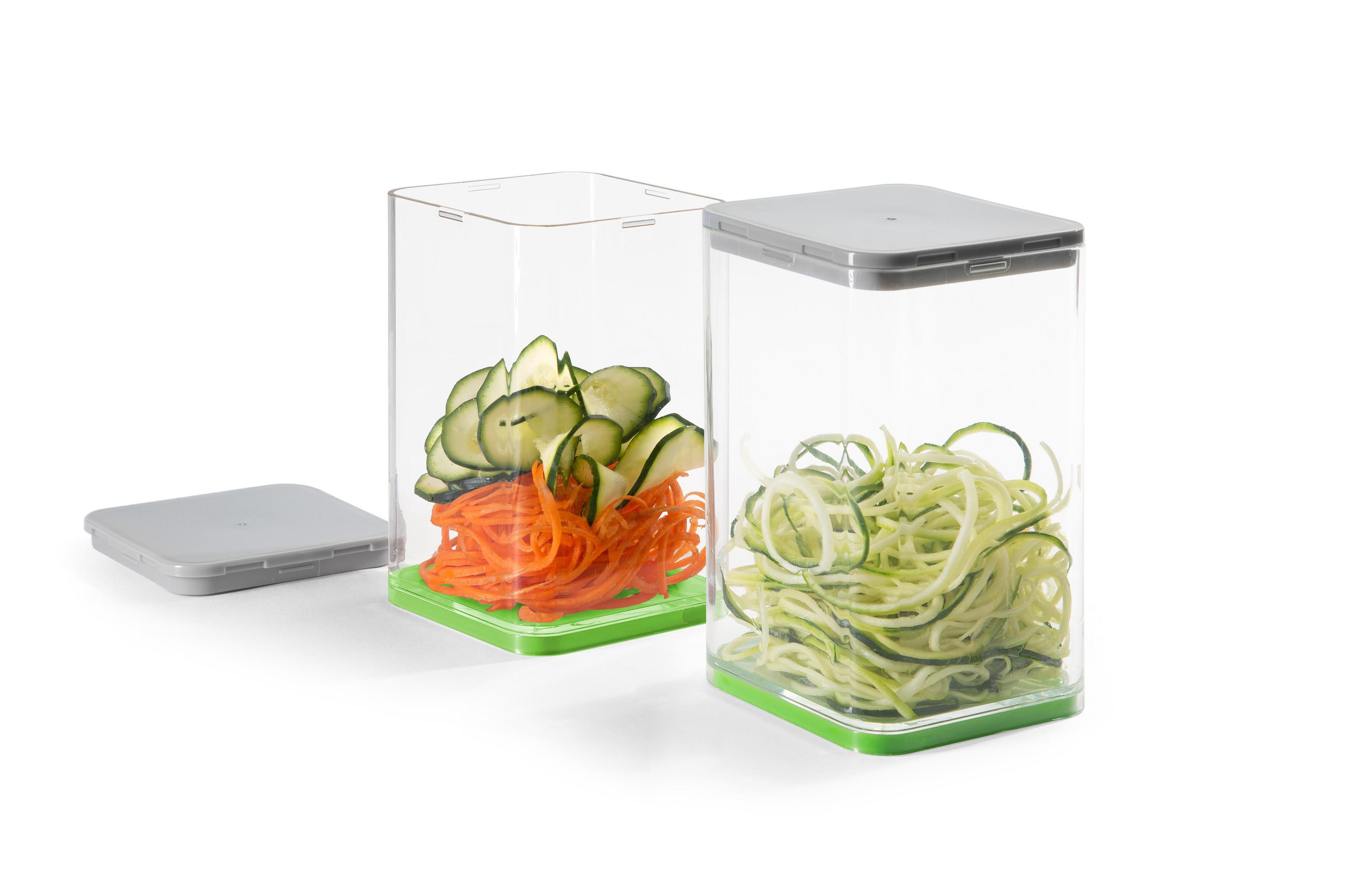 Transparente Lebensmittelbehälter mit grünen Böden, gefüllt mit Karotten und Zucchini.