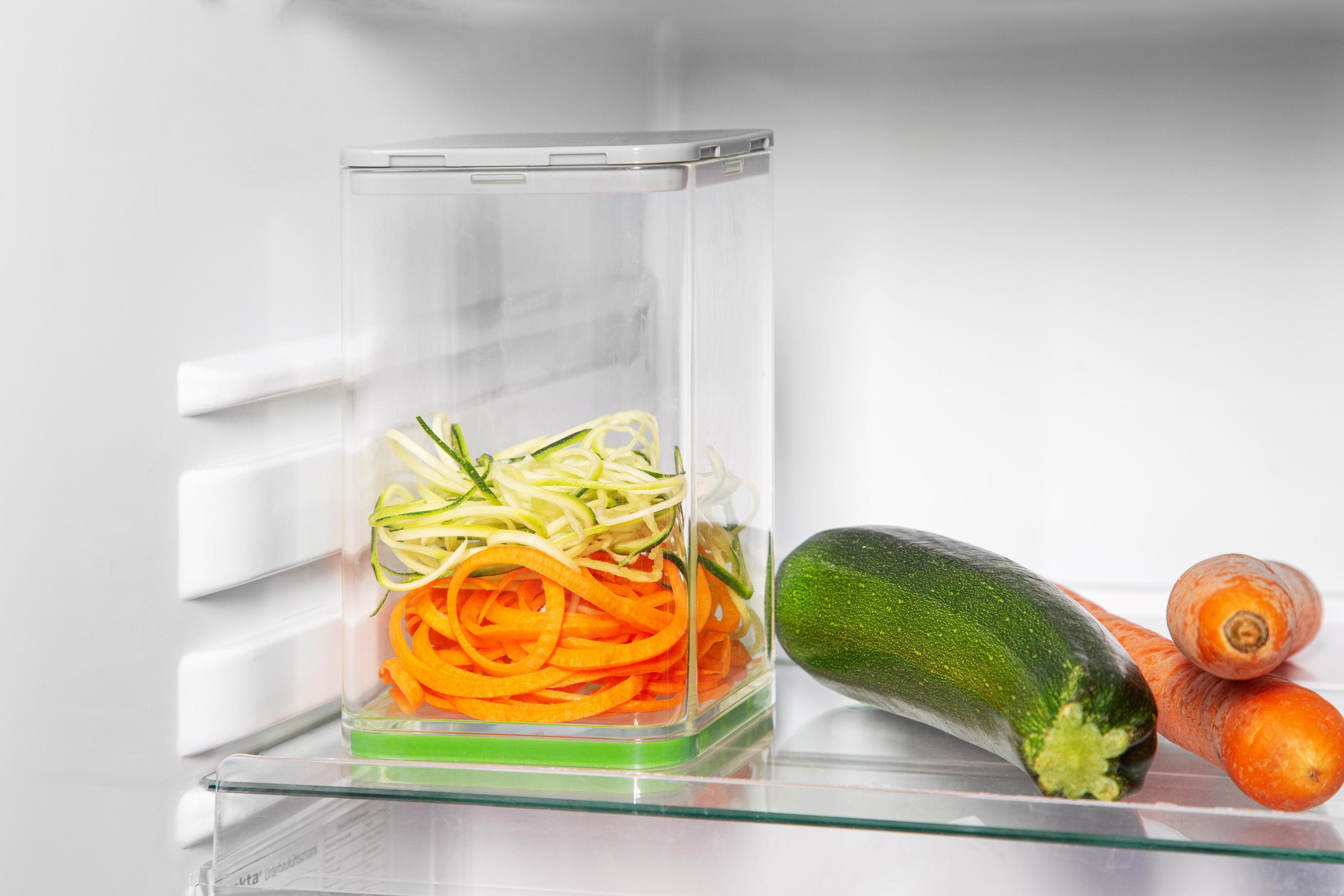 Ein klarer Behälter mit Karotten und Zucchini darin. Zucchini und Karotten liegen daneben.