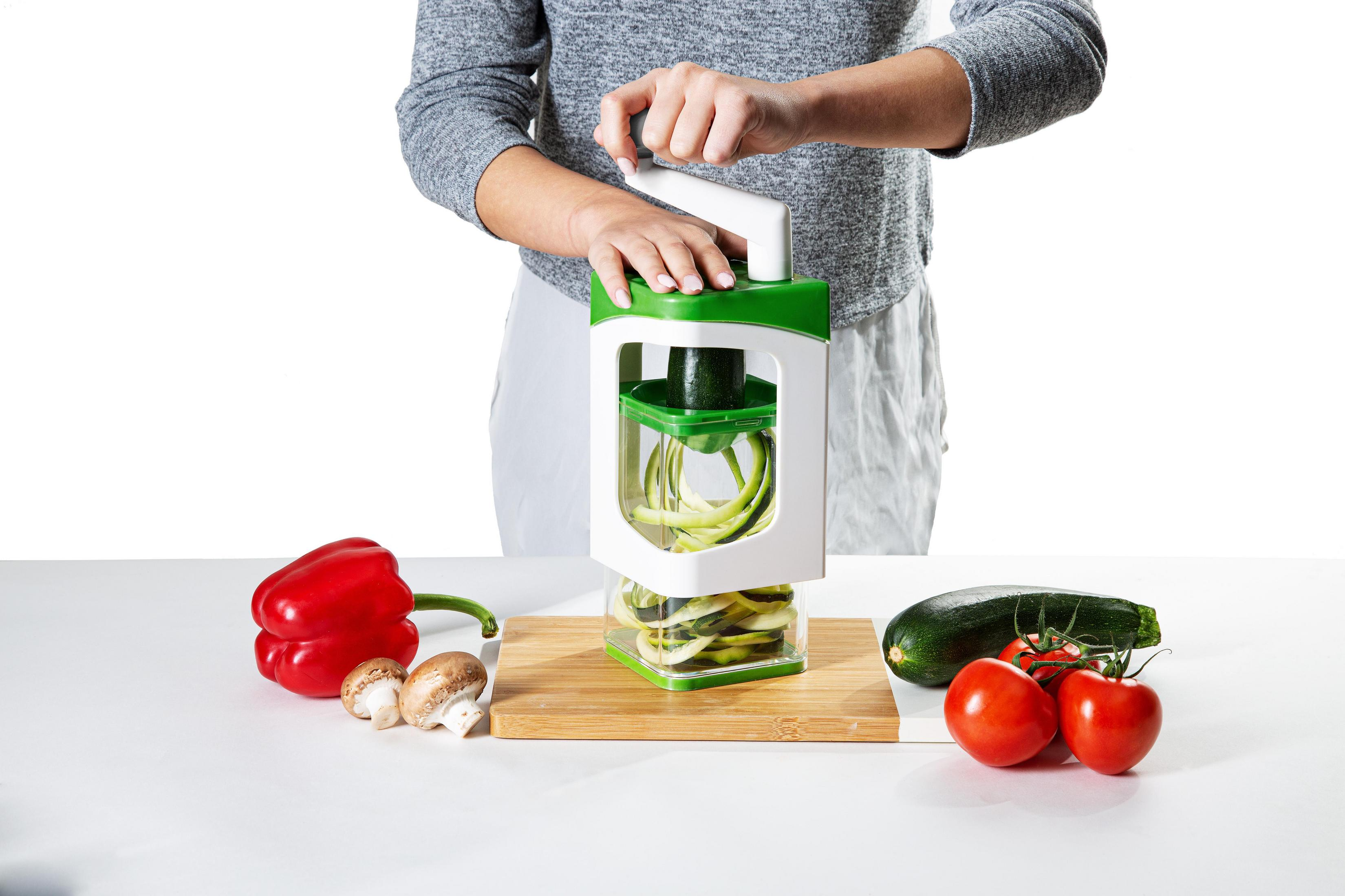 Person benutzt Gemüsespiralschneider. Zucchini und Gemüse auf dem Tisch.