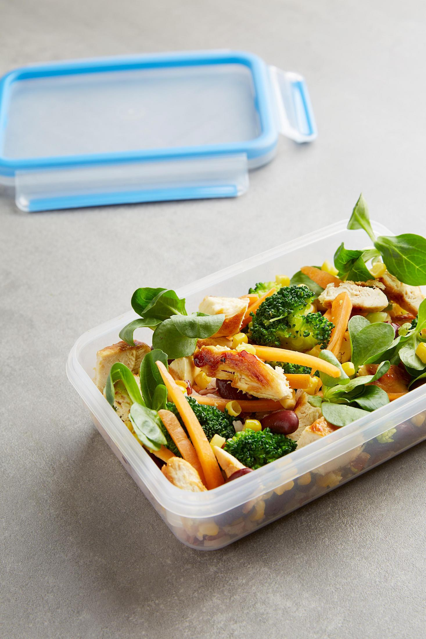 Salat mit Hähnchen, Brokkoli, Karotten und Grünzeug in einem Plastikbehälter. Deckel ist offen.