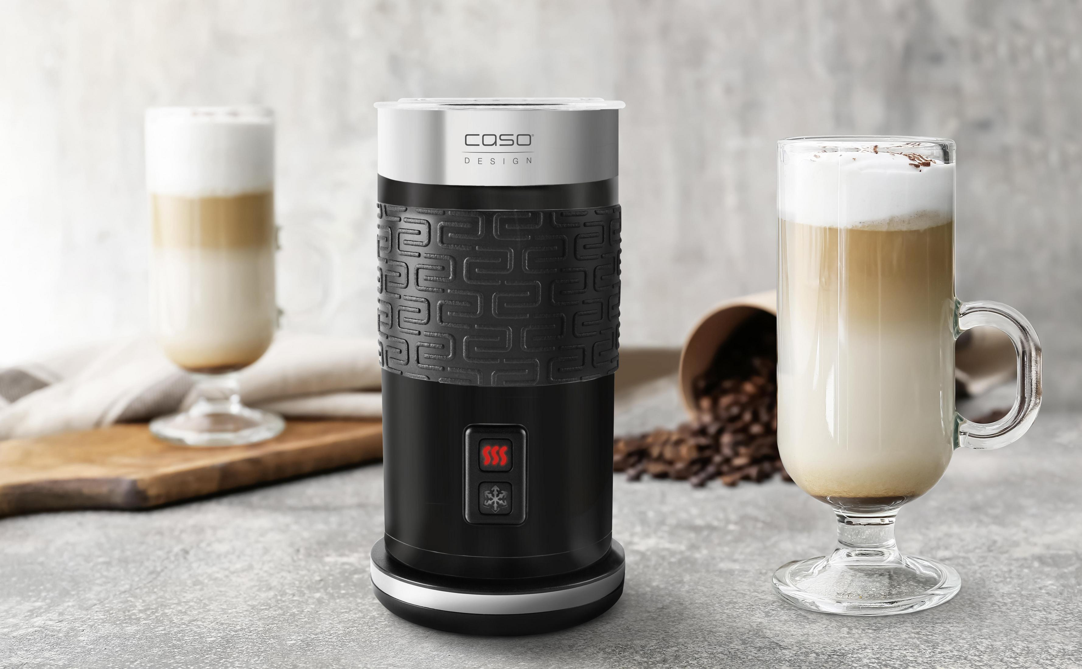 Un montalatte nero e argento con due bicchieri di latte macchiato su una superficie chiara.