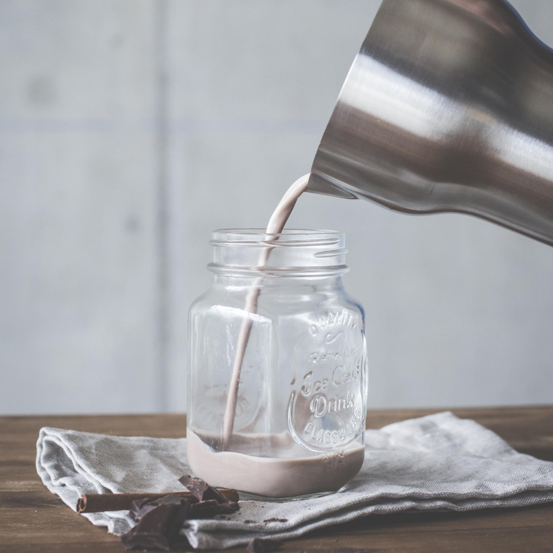 Mleko czekoladowe jest wlewane do słoika. W pobliżu czekolada i laska cynamonu.