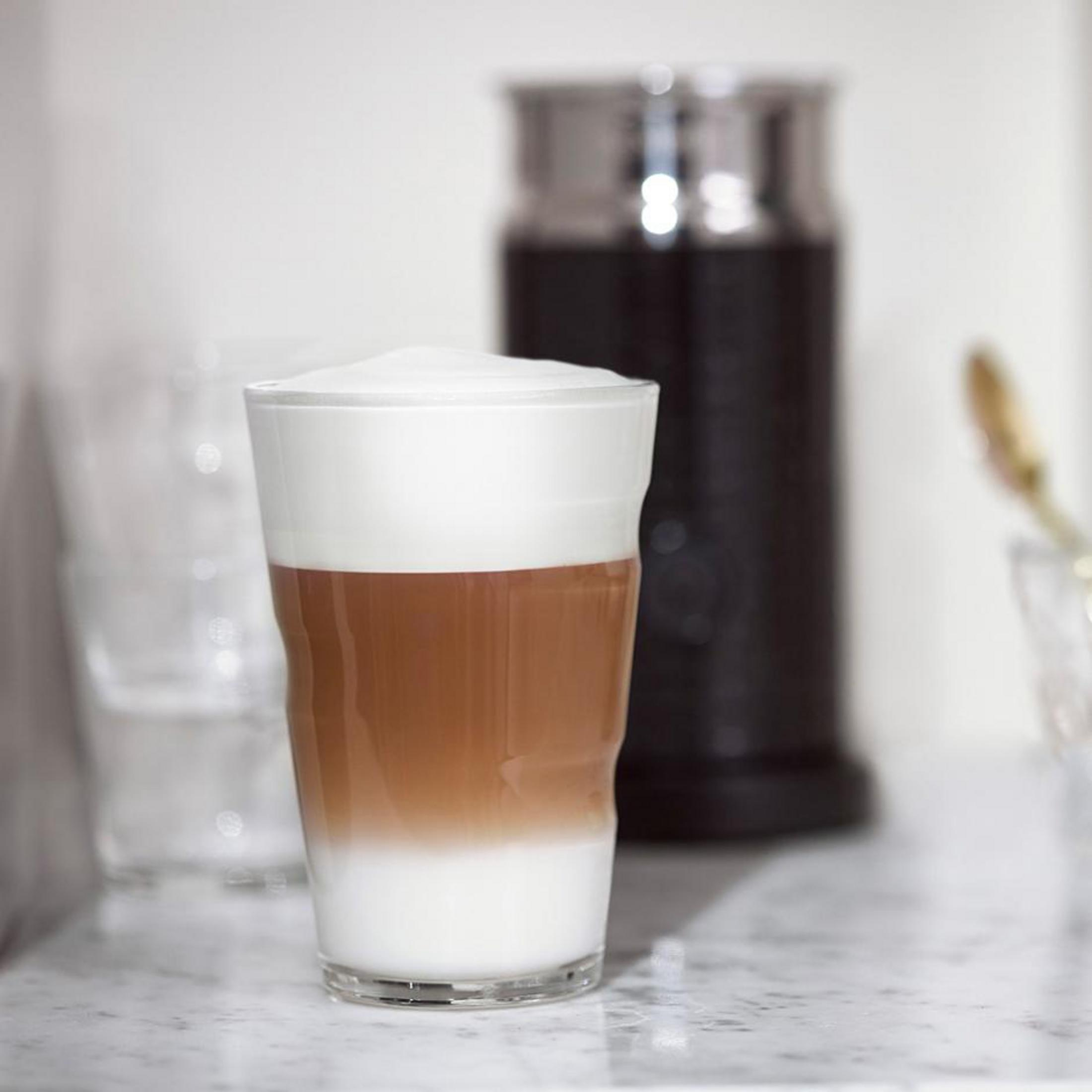 Ein Glas geschichteter Latte. Es zeigt weißen Schaum oben, eine hellbraune Mitte und eine dunklere untere Schicht.