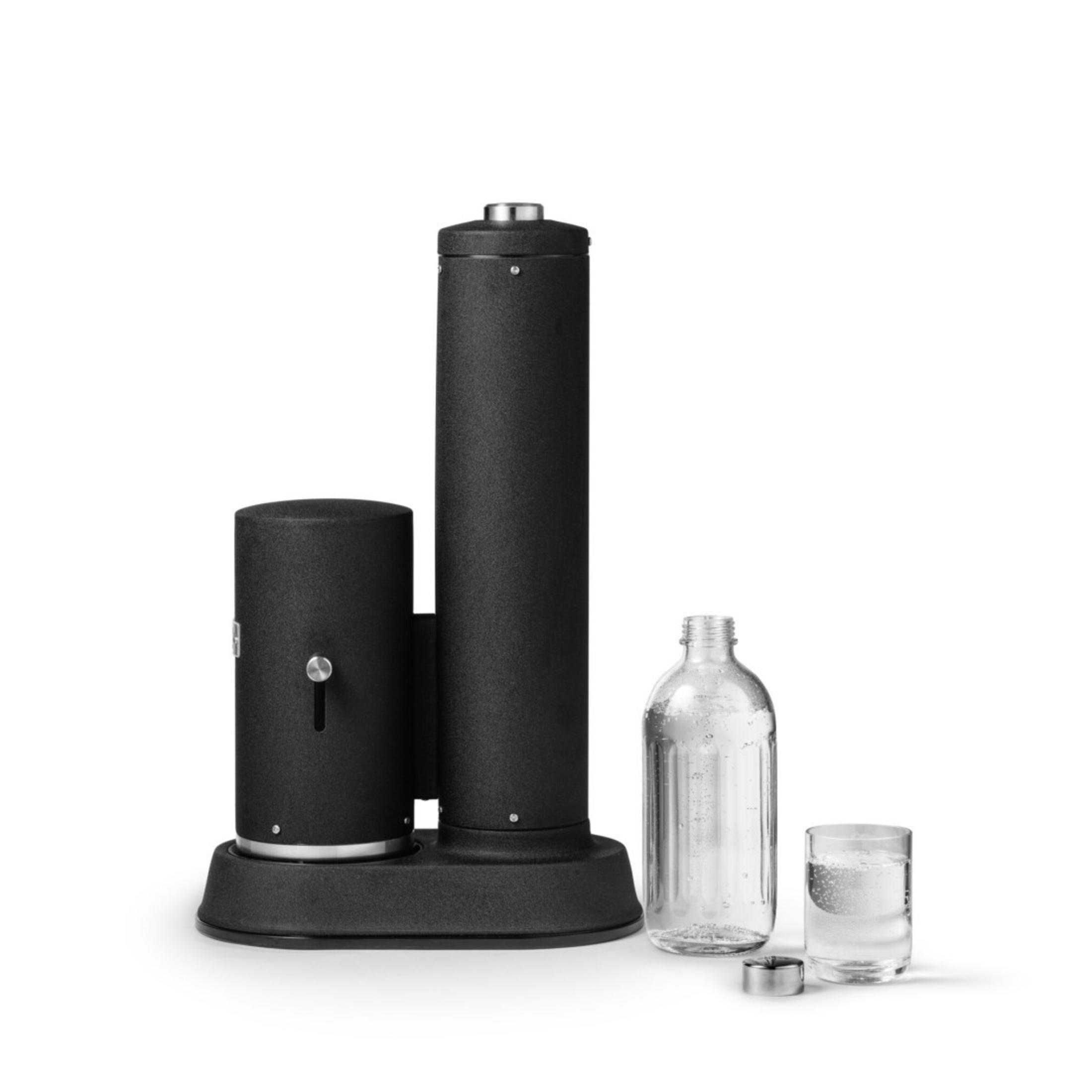 Un produttore di soda nero con una bottiglia trasparente e un bicchiere con bolle accanto, tutto su bianco.
