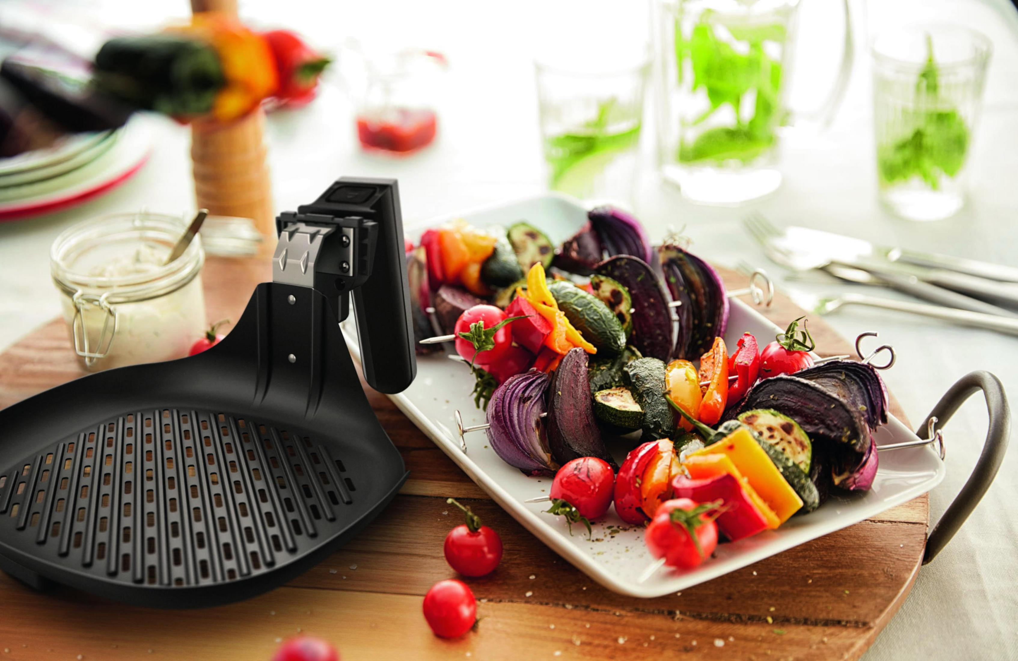 Verduras a la parrilla en brochetas y una sartén para asar en un plato blanco.