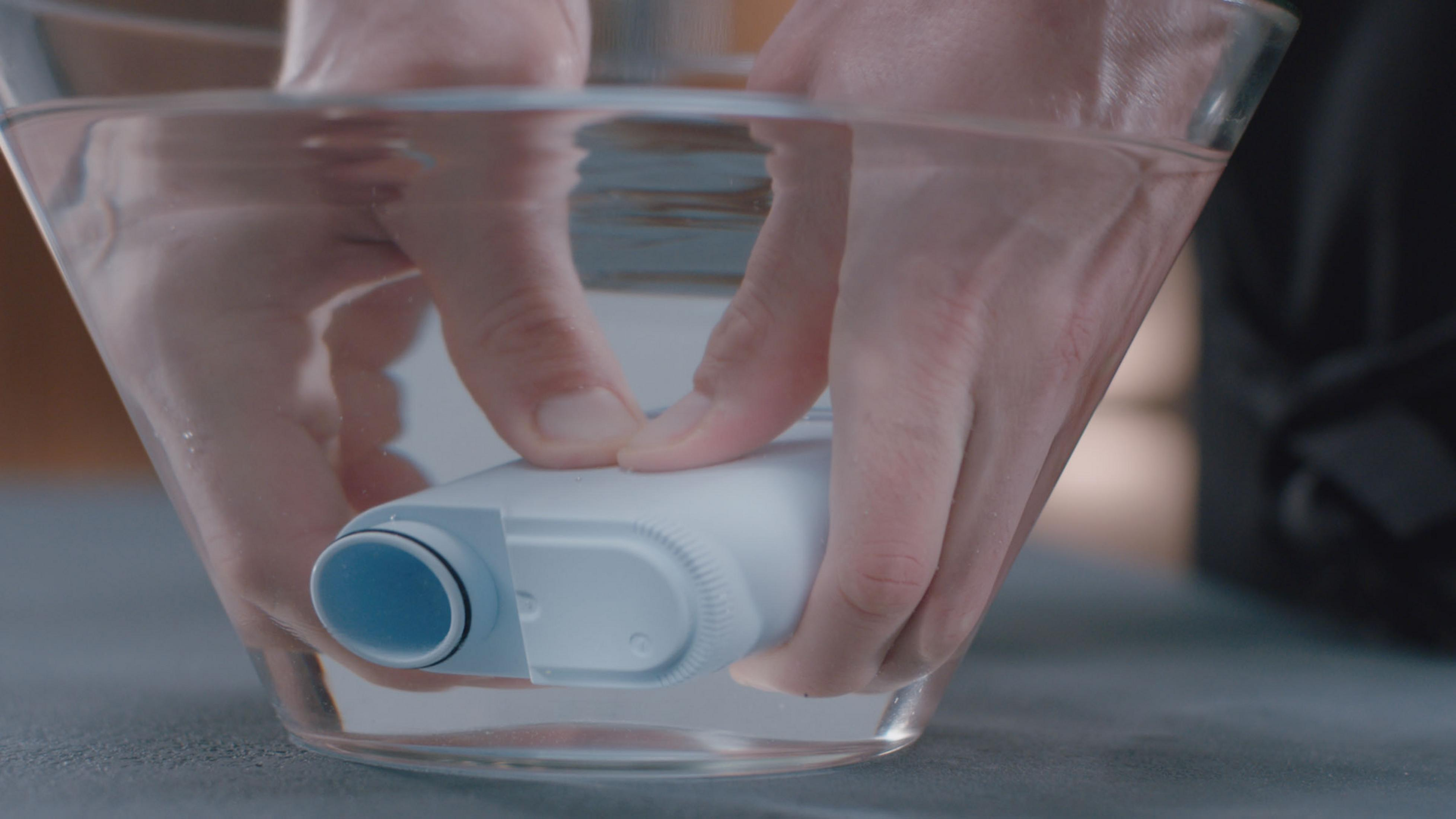 Hände halten einen Wasserfilter in einer mit Wasser gefüllten Glasschüssel.