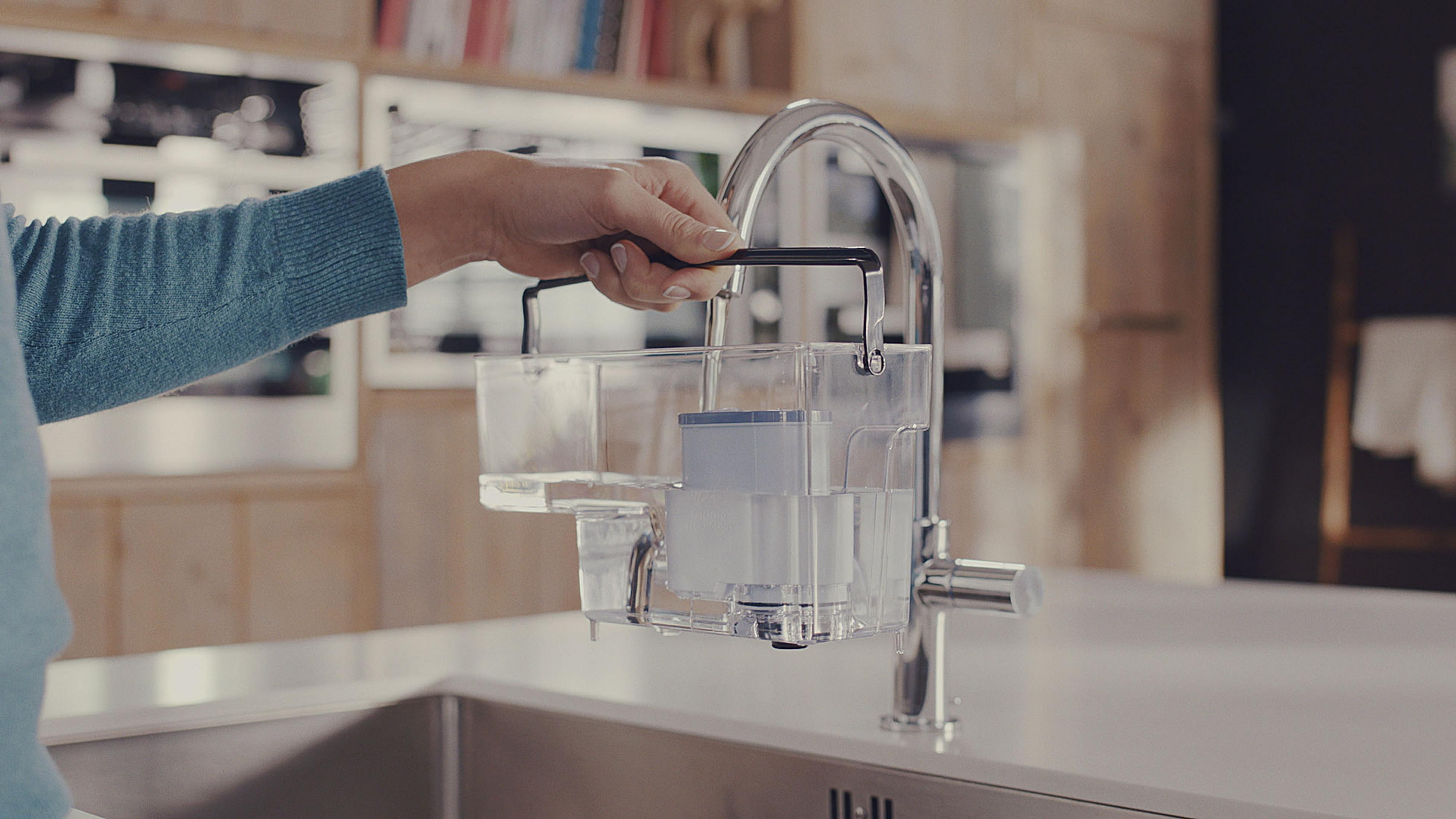 Eine Hand hält einen Wasserfilter. Er besteht aus klarem Kunststoff und ist über einem Waschbecken platziert.