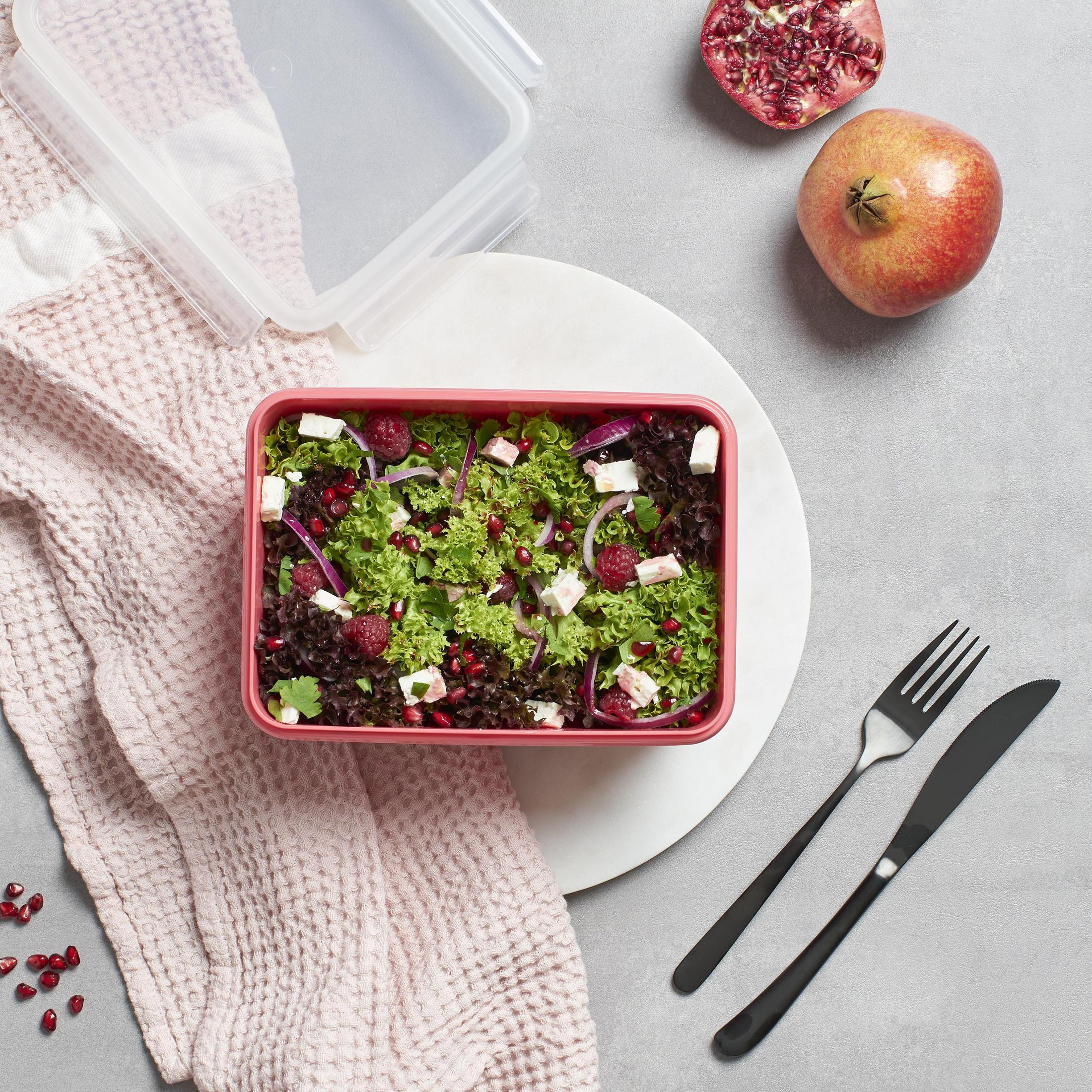Ein Salat in einem rosa Behälter mit Himbeeren, roten Zwiebeln und Feta-Käse, mit Gabel und Messer.