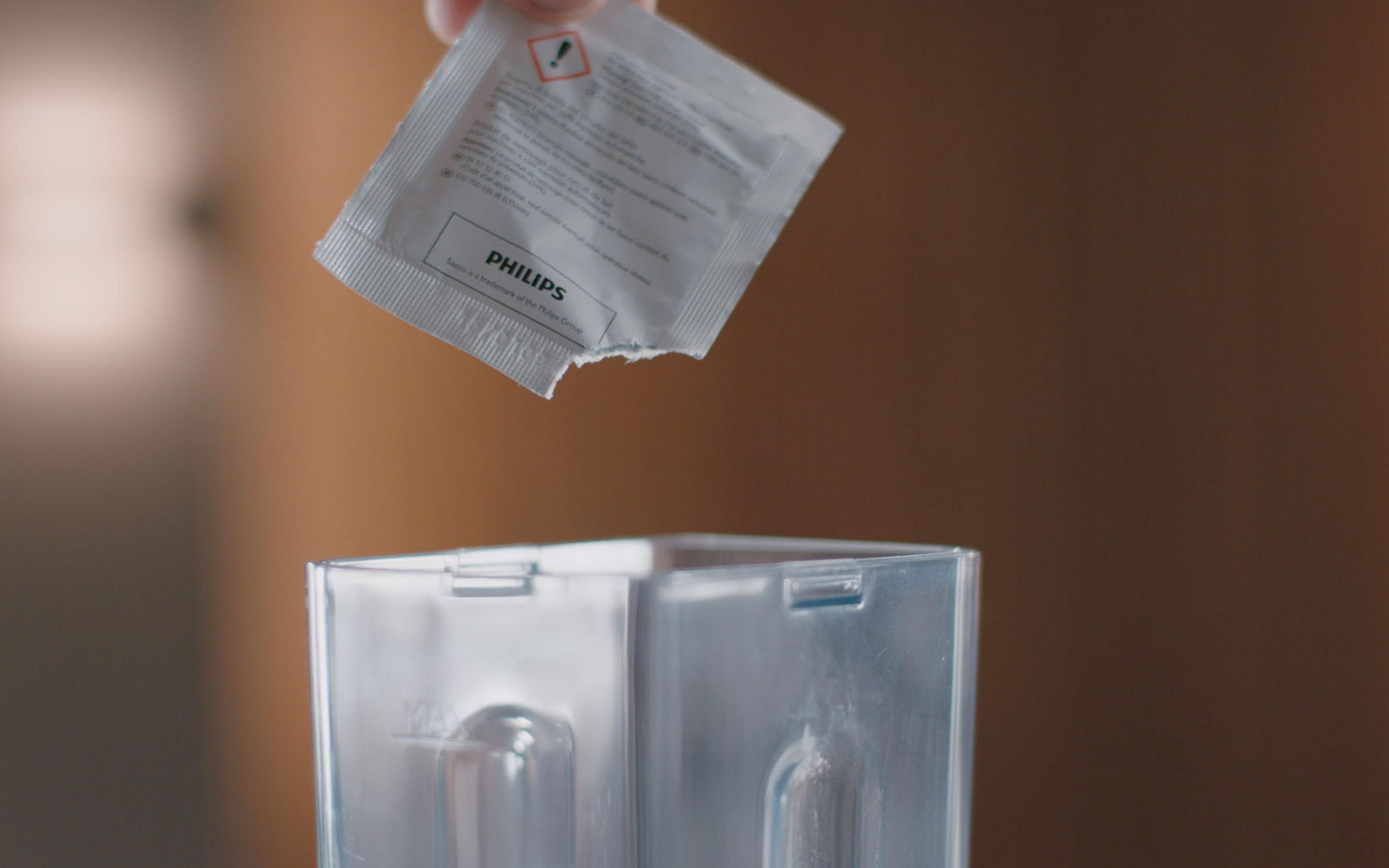 Ręka trzymająca paczkę Philips, upuszczająca ją do przezroczystego pojemnika.